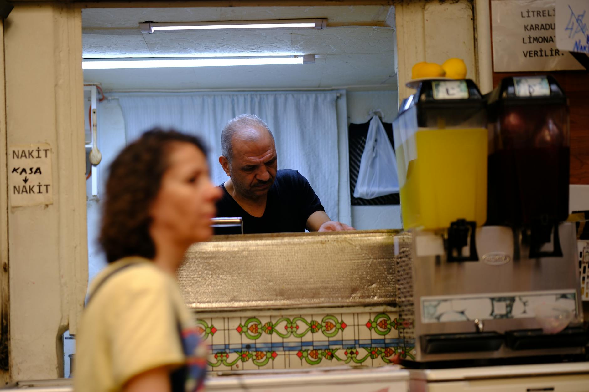 Busy small business environment in İzmir with people and juice dispenser, showcasing local retail setting.