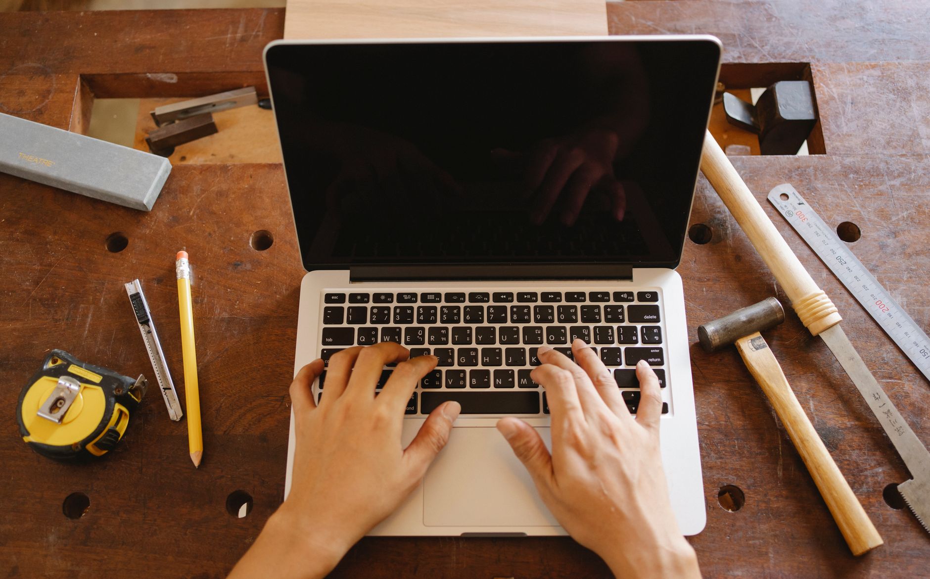 A small business owner working at a laptop surrounded by papers and tools
