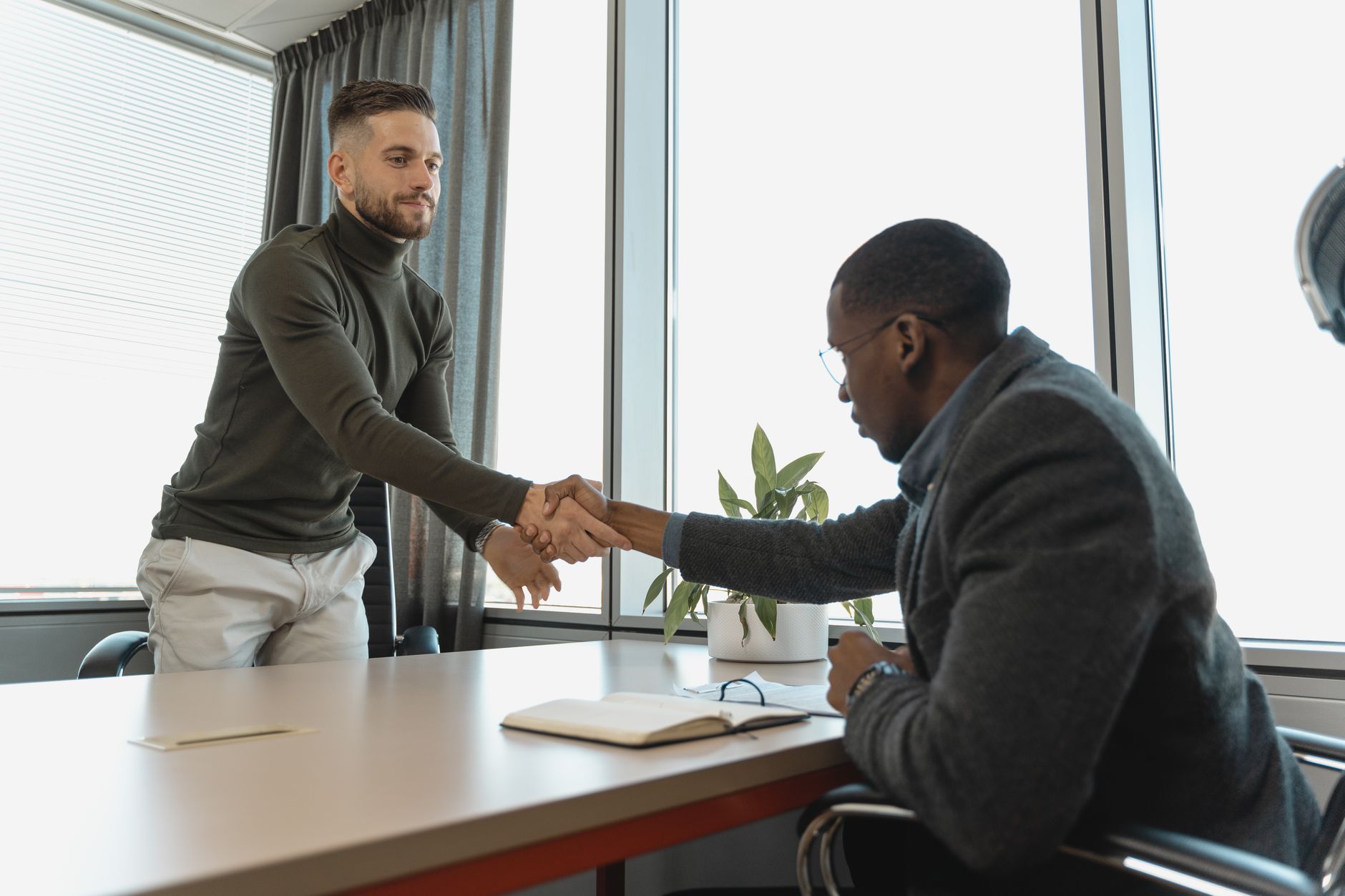 Two business owners shaking hands across a desk, representing a B2B partnership