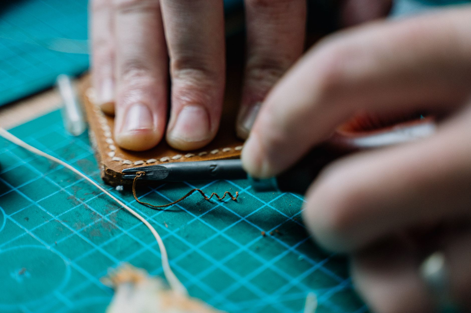 A leatherworker hand-stitching a bag among their tools