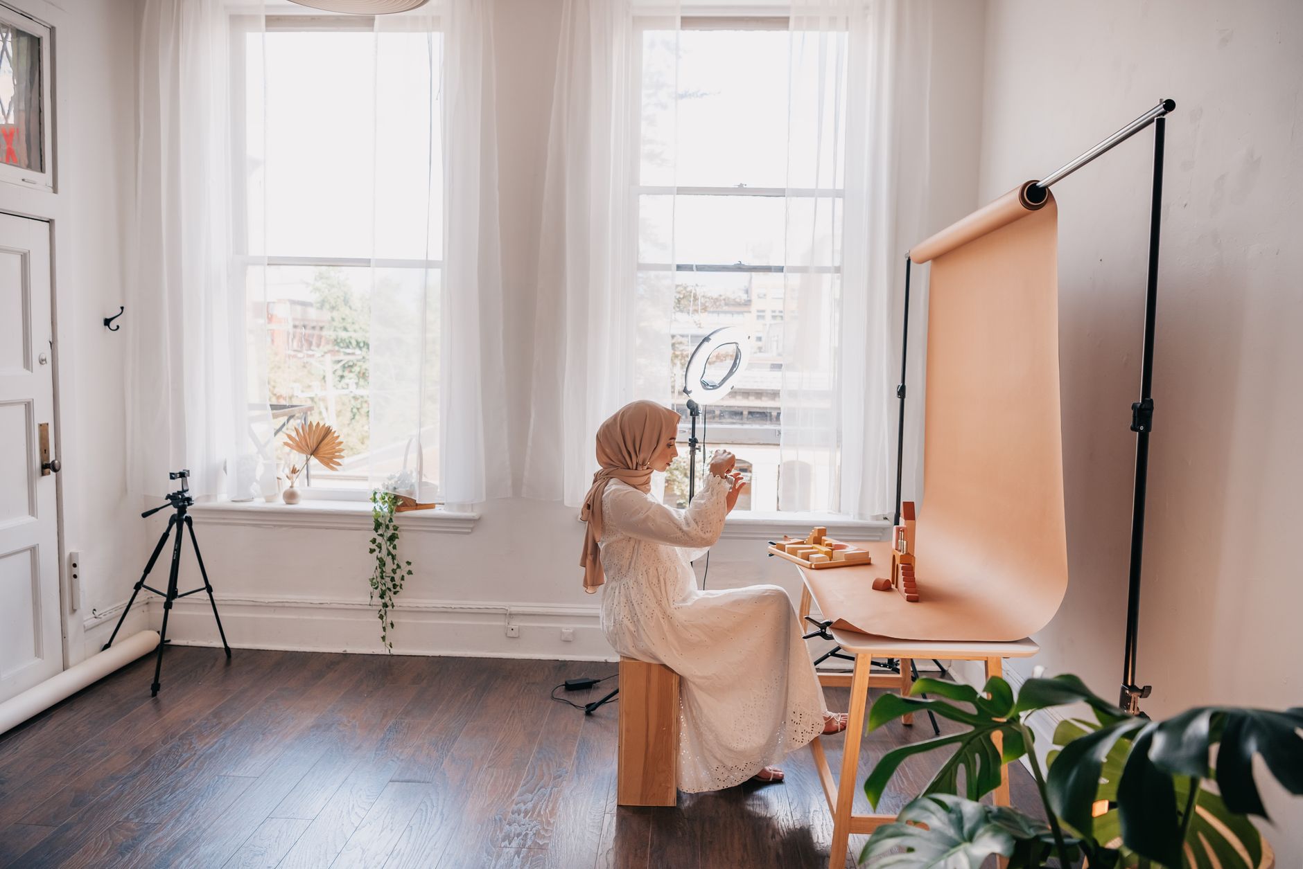 A woman photographing a handmade product by a bright window for her shop