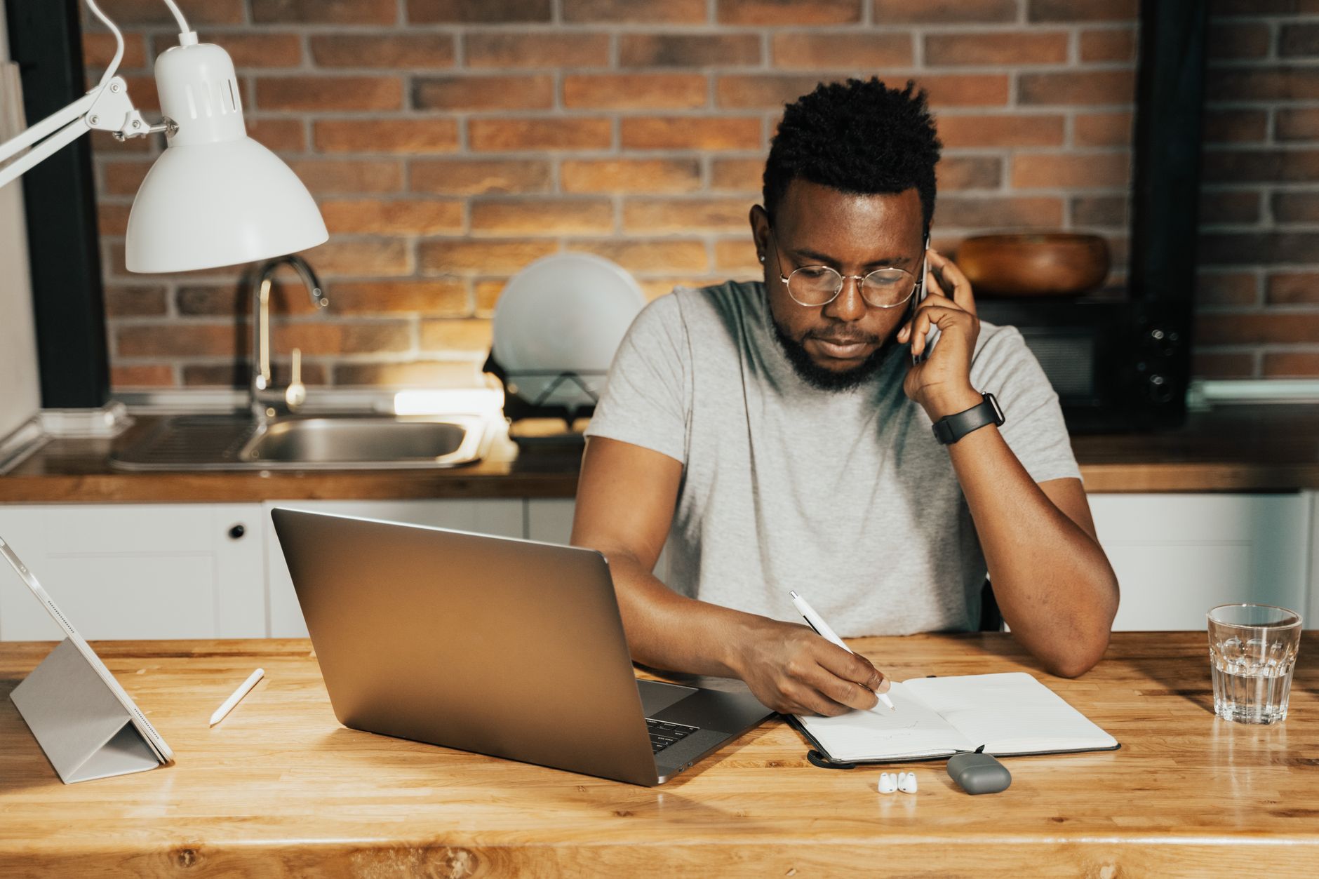 A person writing at a laptop at a kitchen table