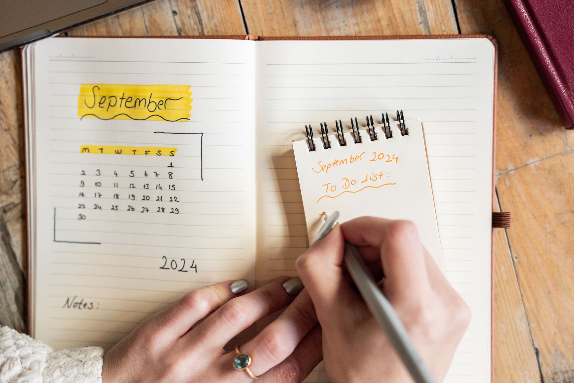 A person planning the months ahead with a notebook and wall calendar at a desk