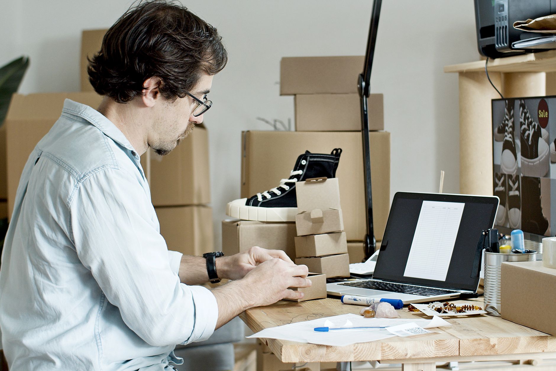 A maker packing small product orders into boxes at a table at home