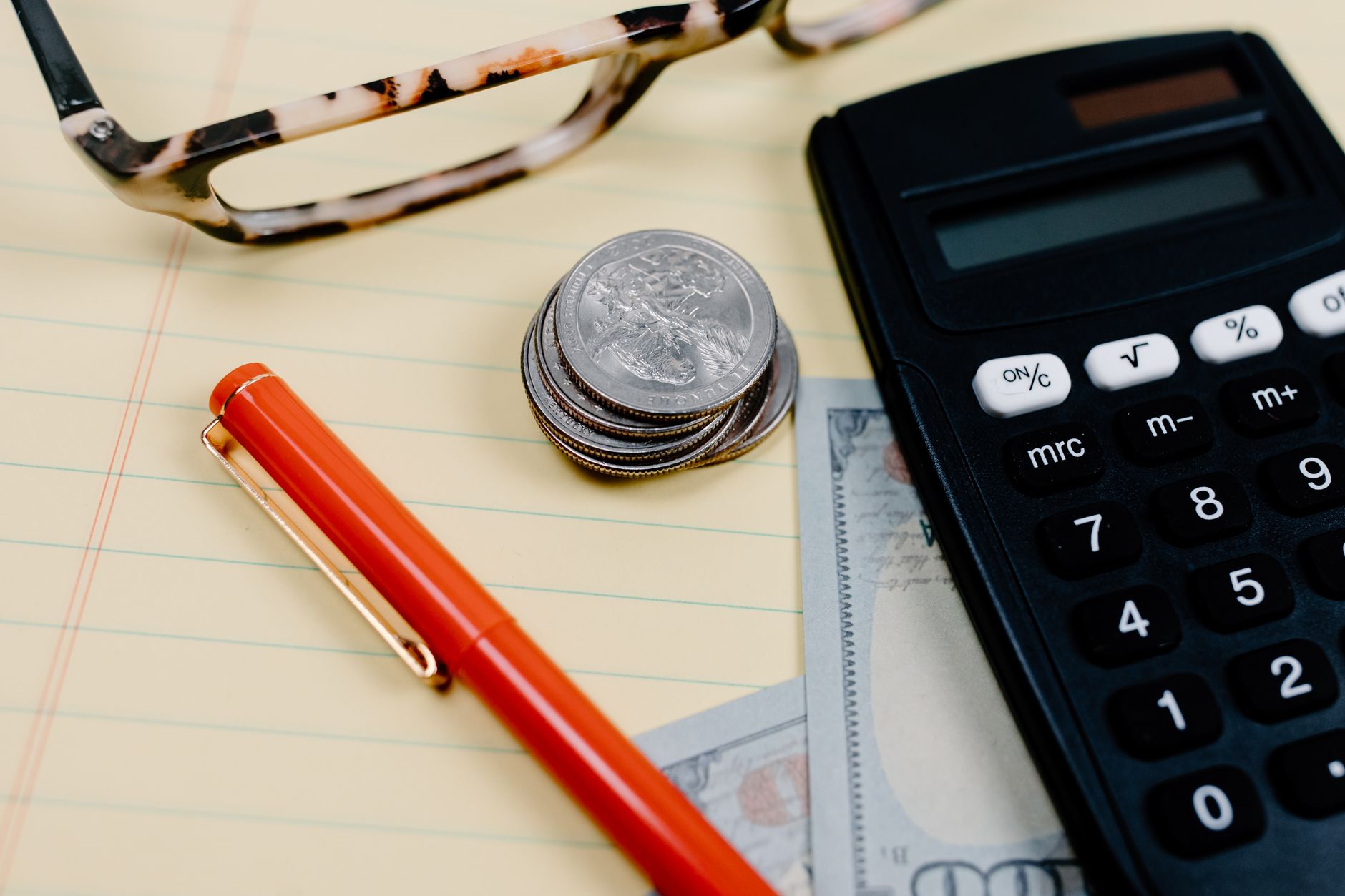 A person writing start up costs in a notebook beside a calculator and a small stack of coins