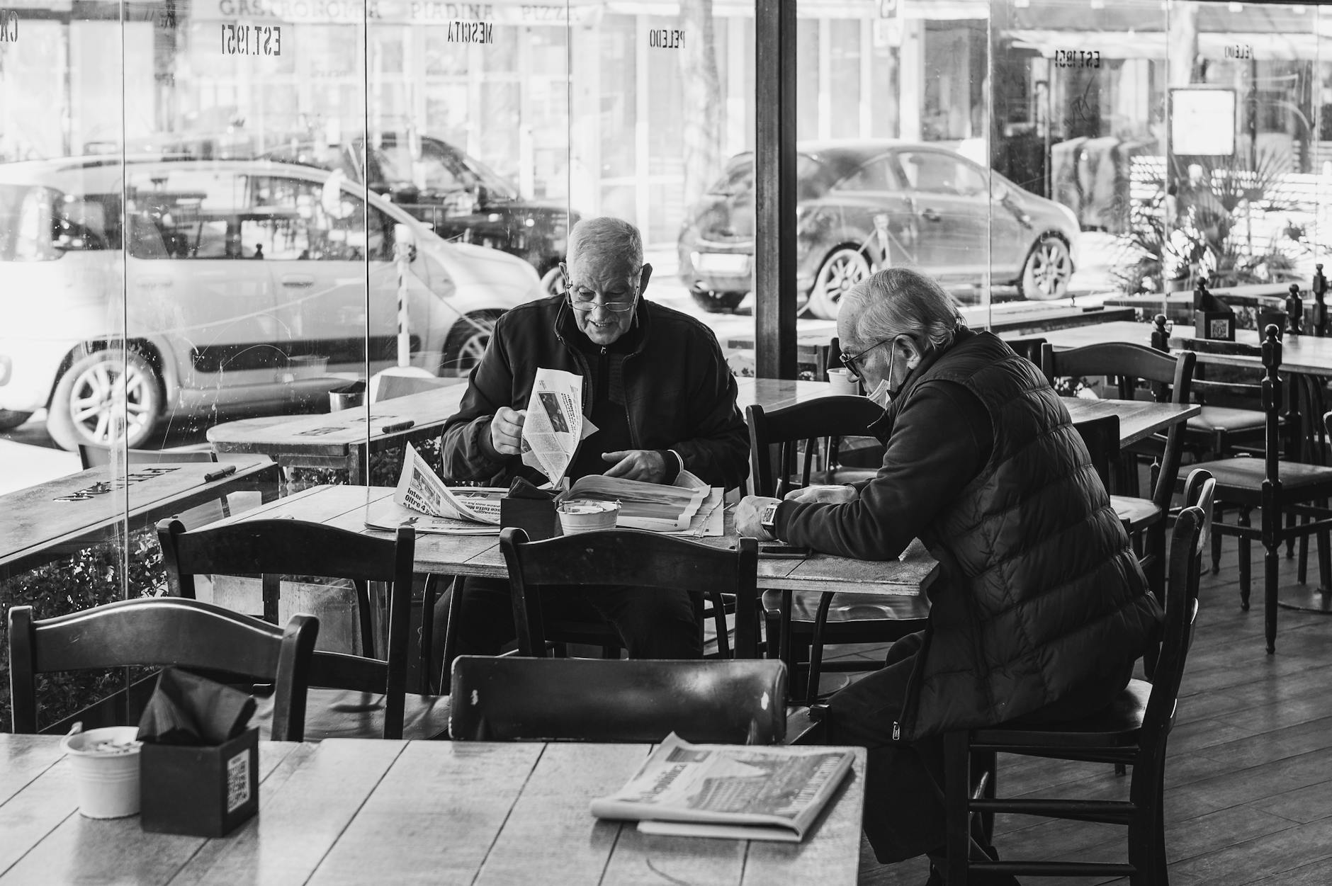 Two senior adults reading newspapers in a Rimini cafe, Italy.