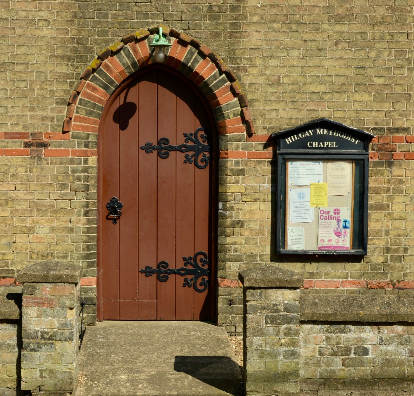A community noticeboard in a village hall covered with local flyers and a parish newsletter advertising nearby services.