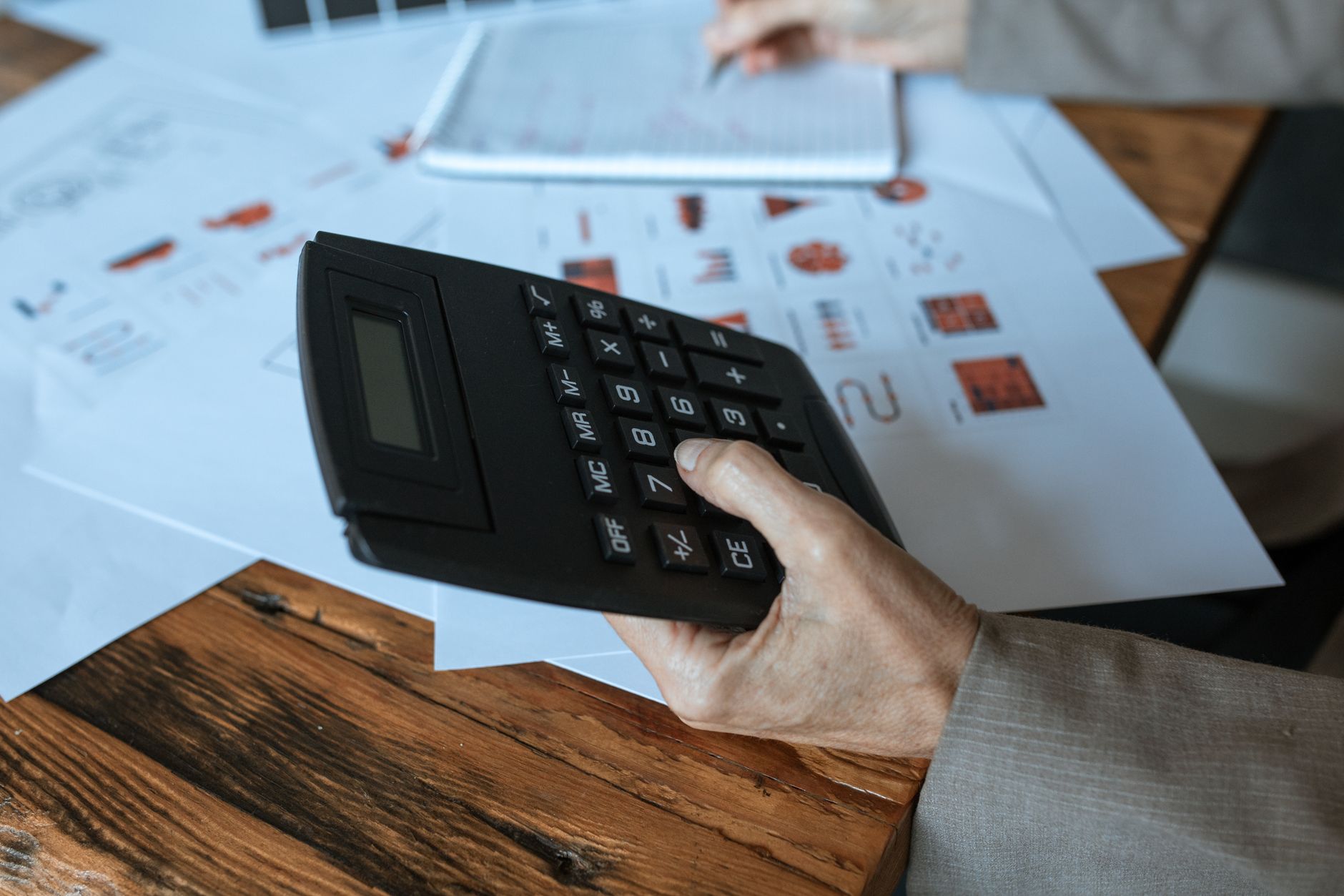 A small business owner sits at a desk working out a monthly advertising budget with a calculator and a notebook of figures.