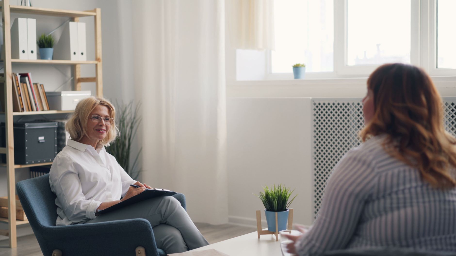 A counsellor and client sitting and talking calmly in a softly lit consulting room, conveying trust and confidentiality
