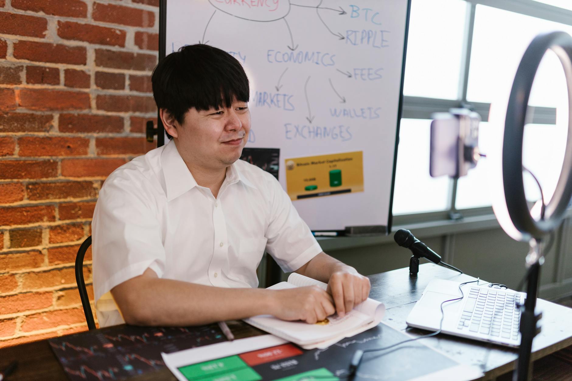 Man engaged in cryptocurrency blogging, using a ring light, microphone, and laptop, with a focus on Bitcoin and trading.