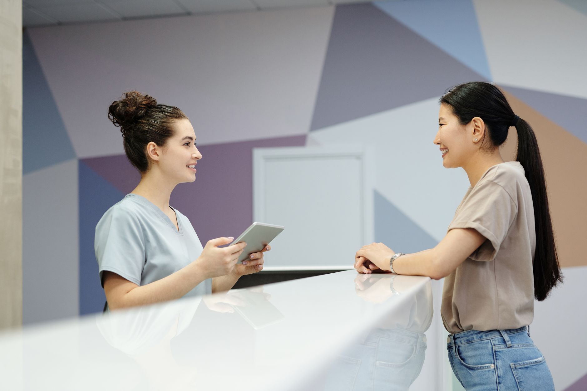 A massage therapist chats warmly with a client at a reception desk, arranging the next appointment in a diary.