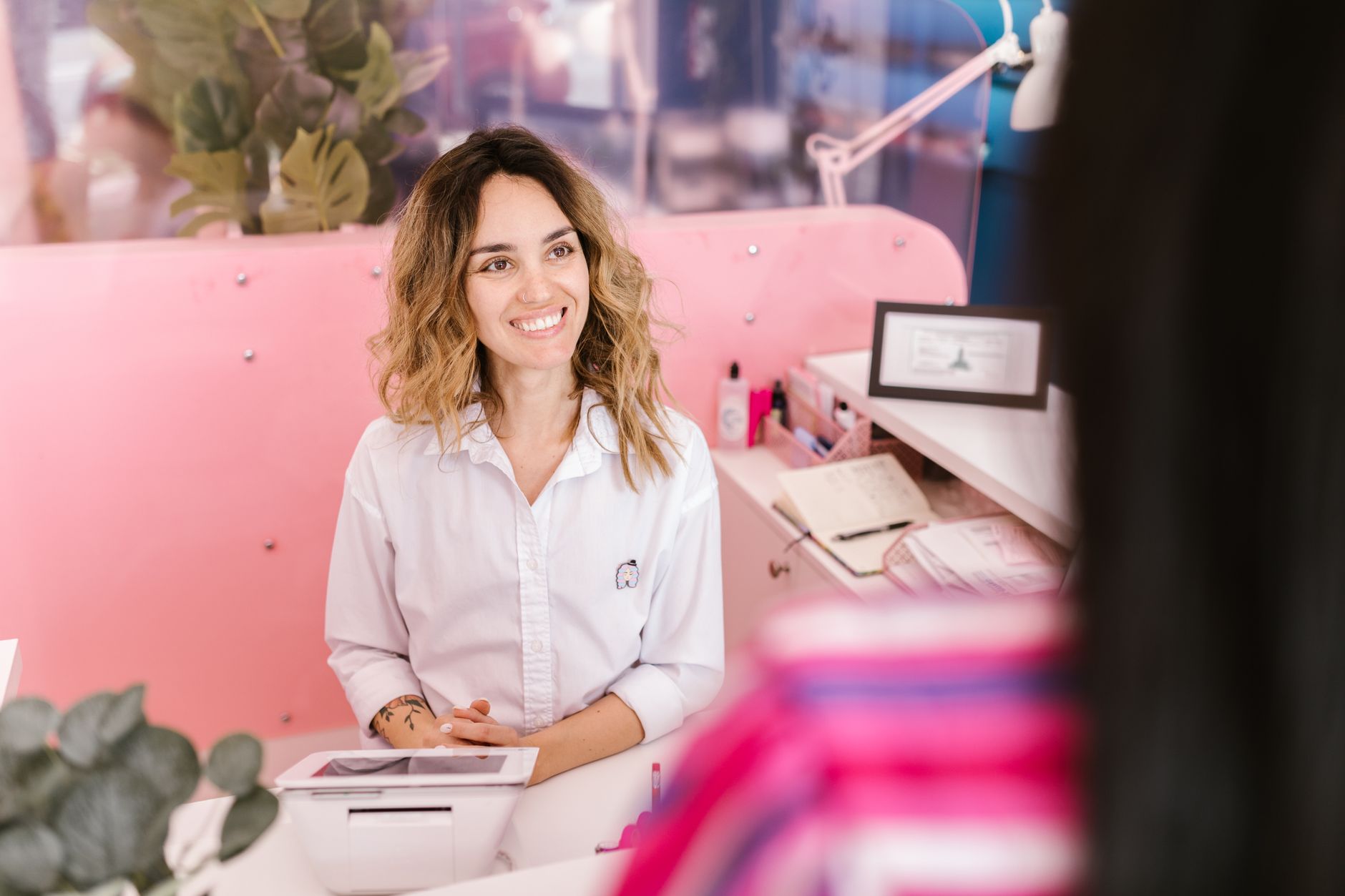 A happy client smiles and chats at a wellness studio reception, the kind of visitor who recommends a therapist to friends.