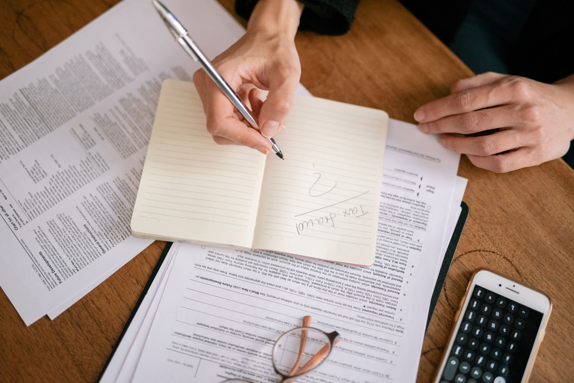 A business owner reviews monthly enquiry figures with a calculator and a handwritten notebook, working out her conversion rate.