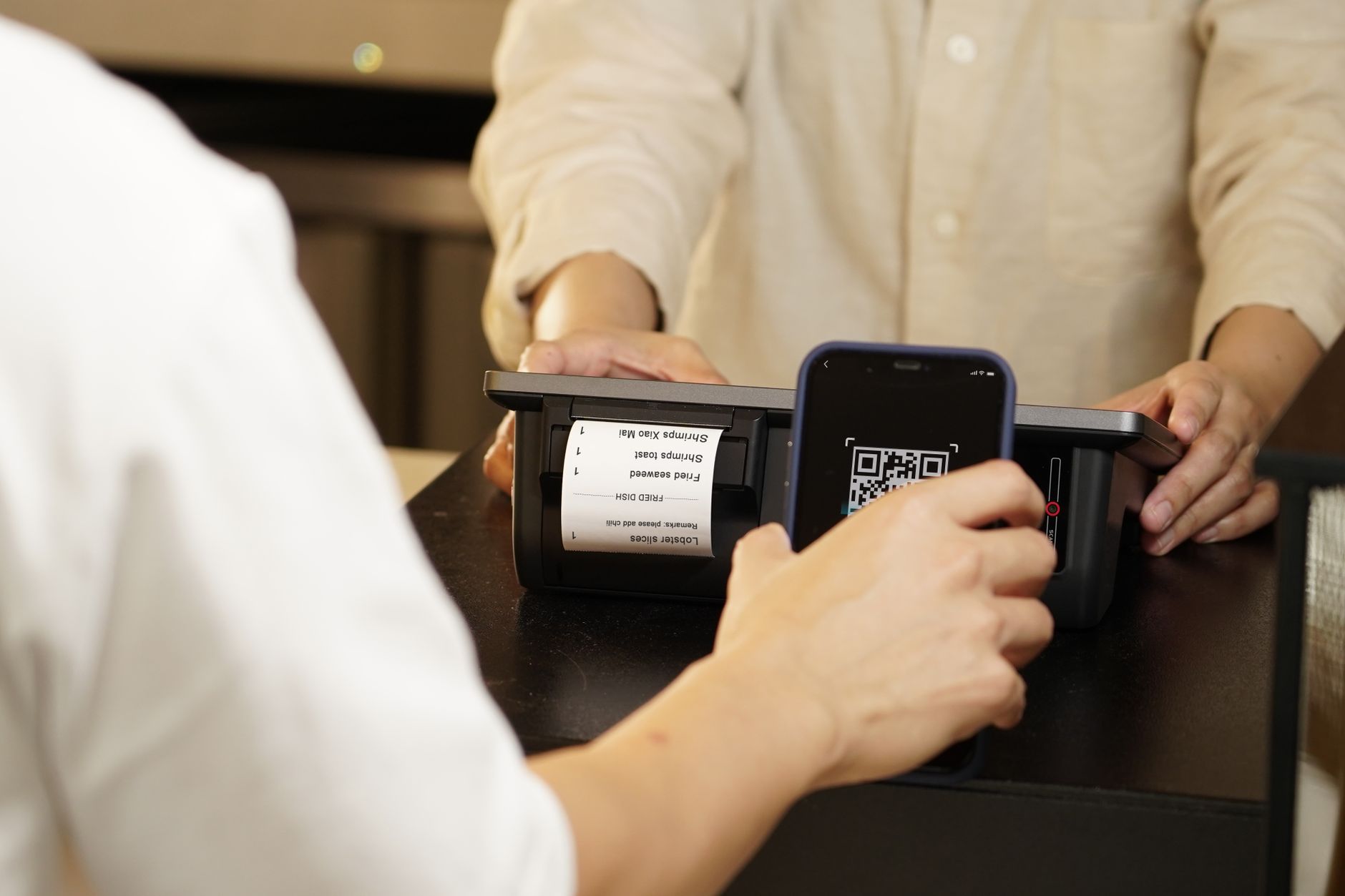 QR code sticker displayed on a shop counter beside a receipt and card machine for easy customer scanning