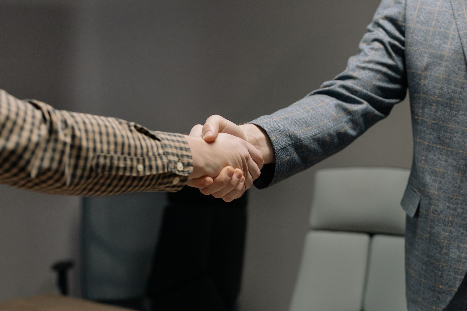 Two small business owners shake hands across a counter, agreeing to refer customers to one another's services.