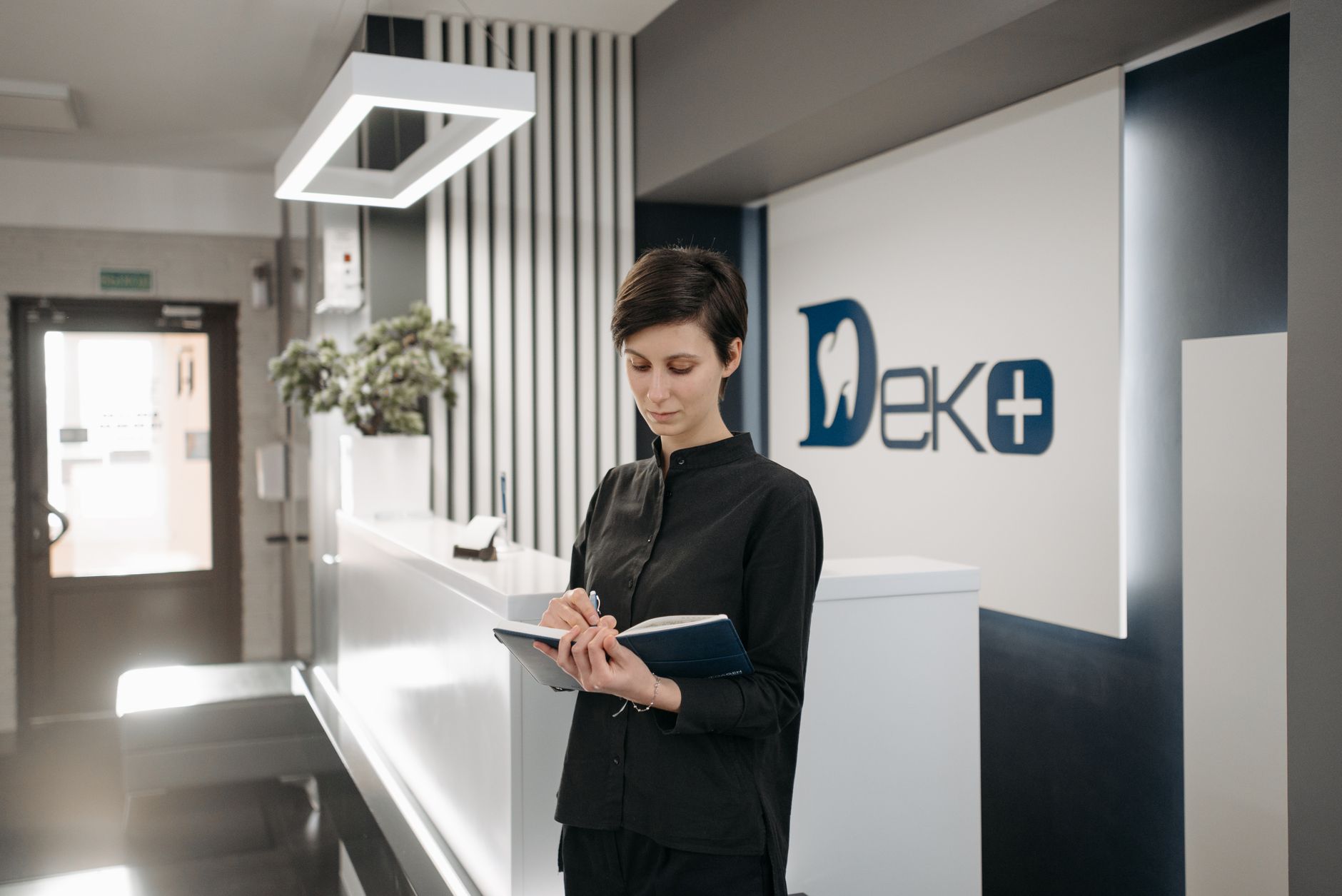 A member of clinic staff reviews the appointment schedule on a tablet at a calm reception desk.