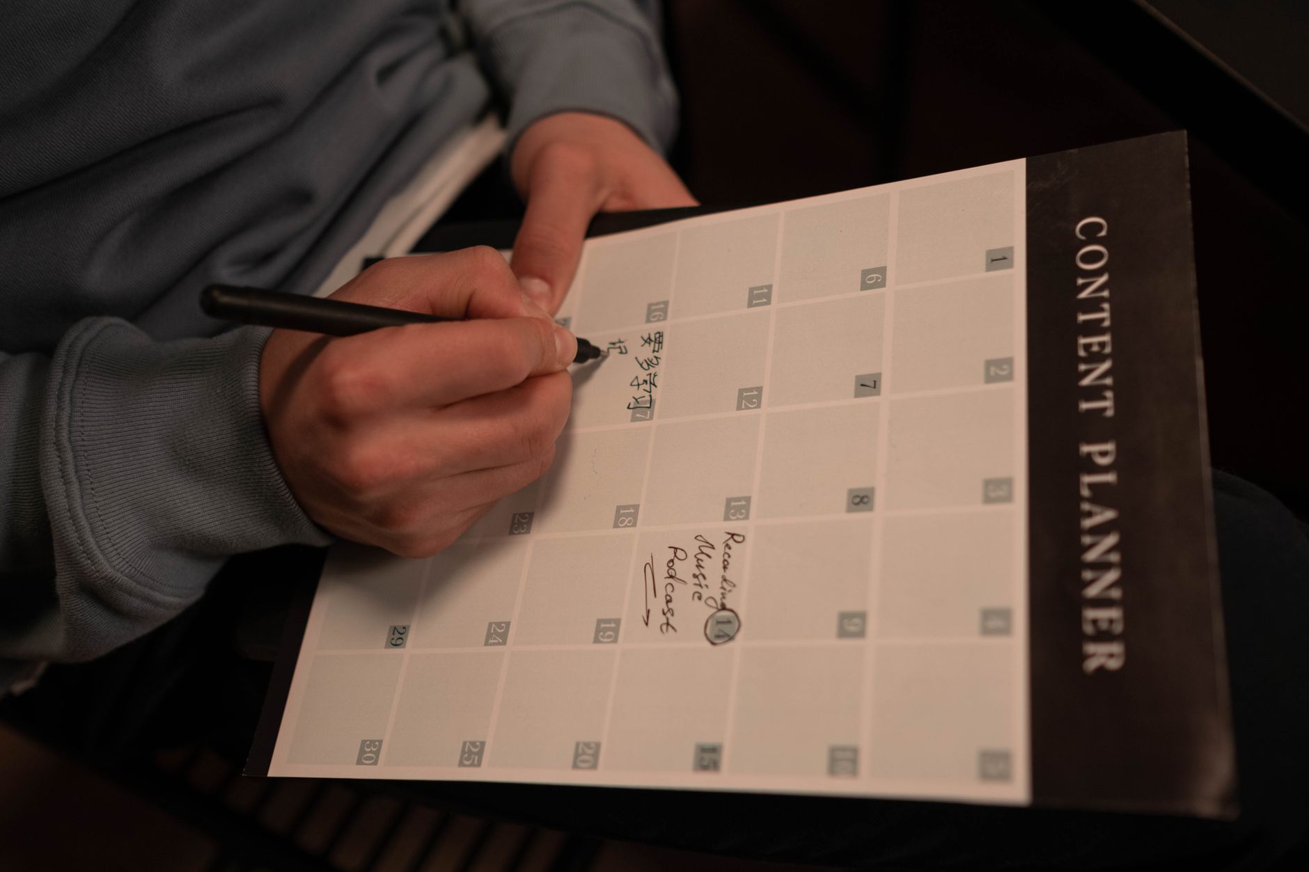 A small business owner plans a week of video ideas on a wall calendar beside a phone and tripod, batching content to stay consistent.