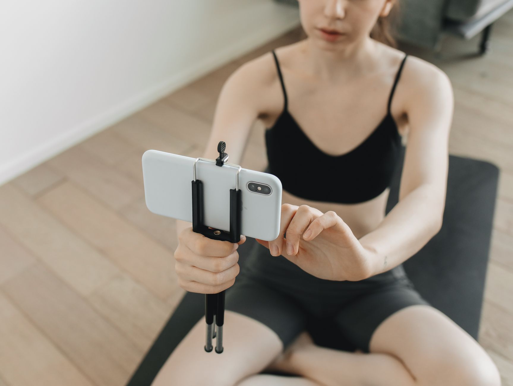 A personal trainer films a short workout demonstration on a phone tripod to post on social media for their followers.