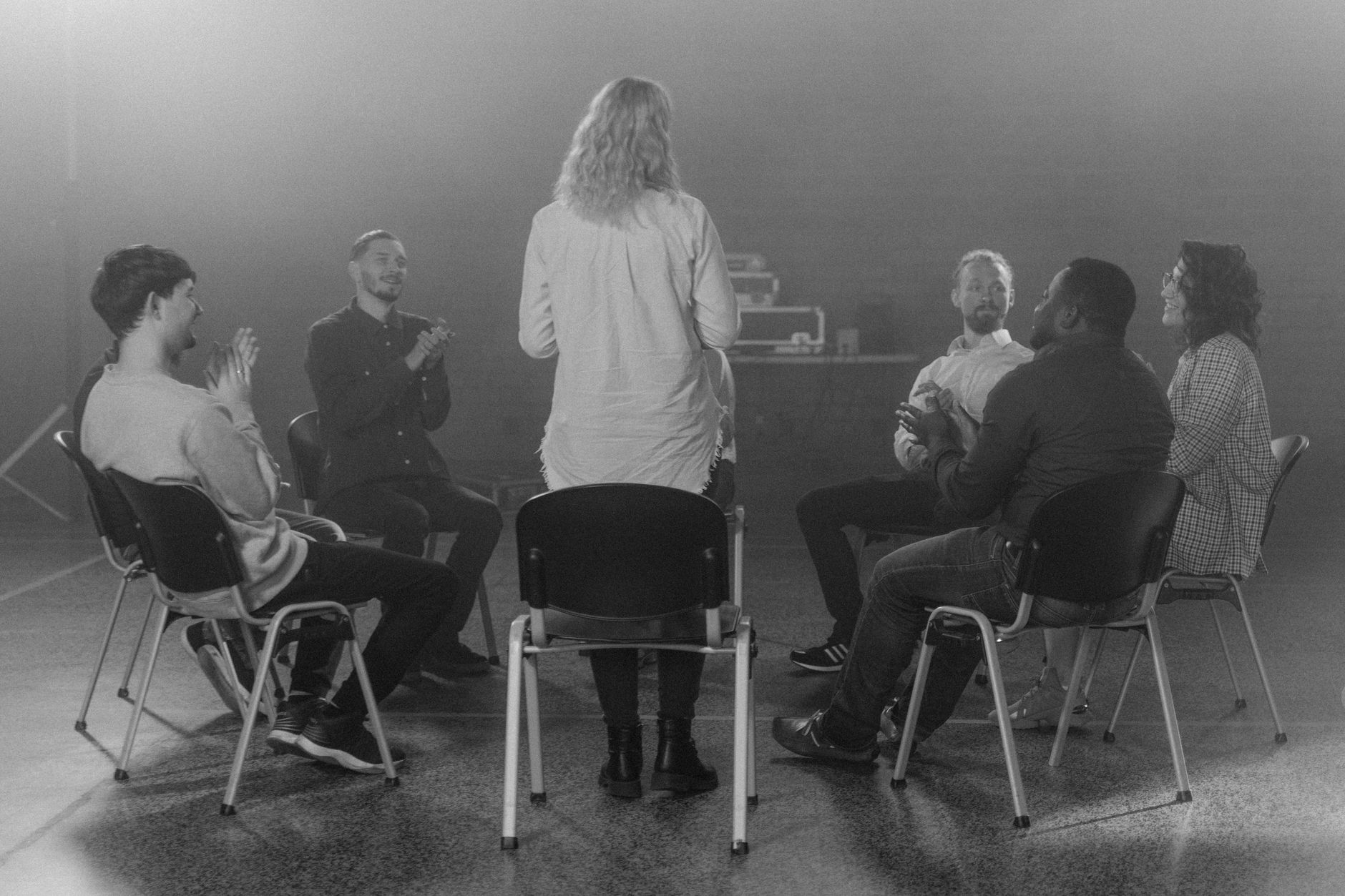 A coach leads a small group programme with six clients seated in a circle, all engaged in a structured group session.