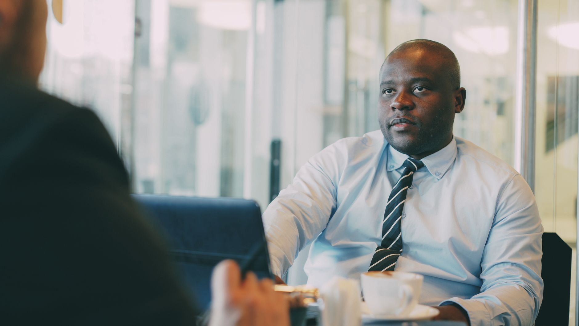 A startup founder leans in during a one-to-one customer interview over coffee, taking notes on a laptop as the customer describes their problem.