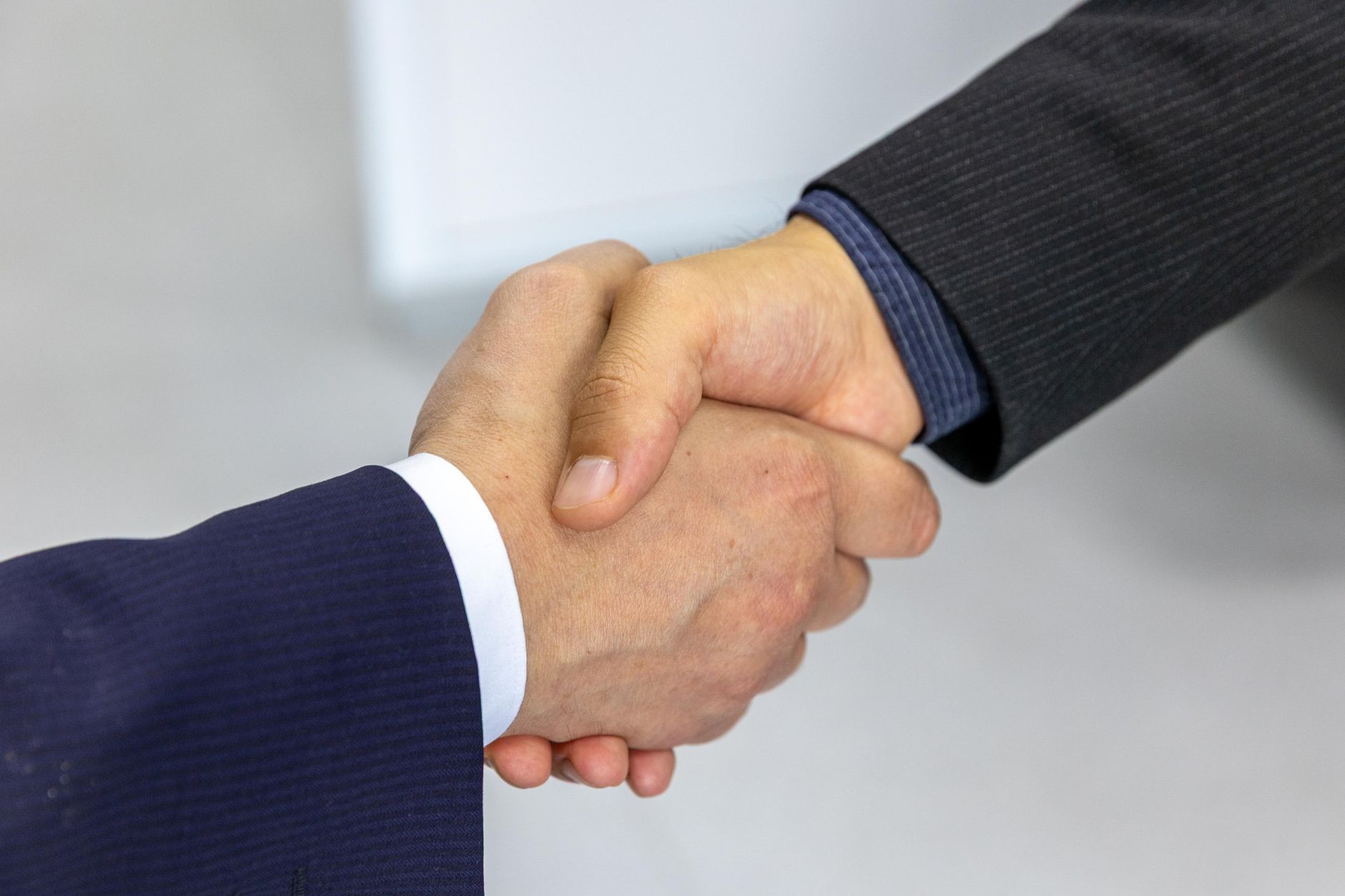Two founders shake hands across a small meeting table after agreeing a joint guide, laptops and coffee cups between them.