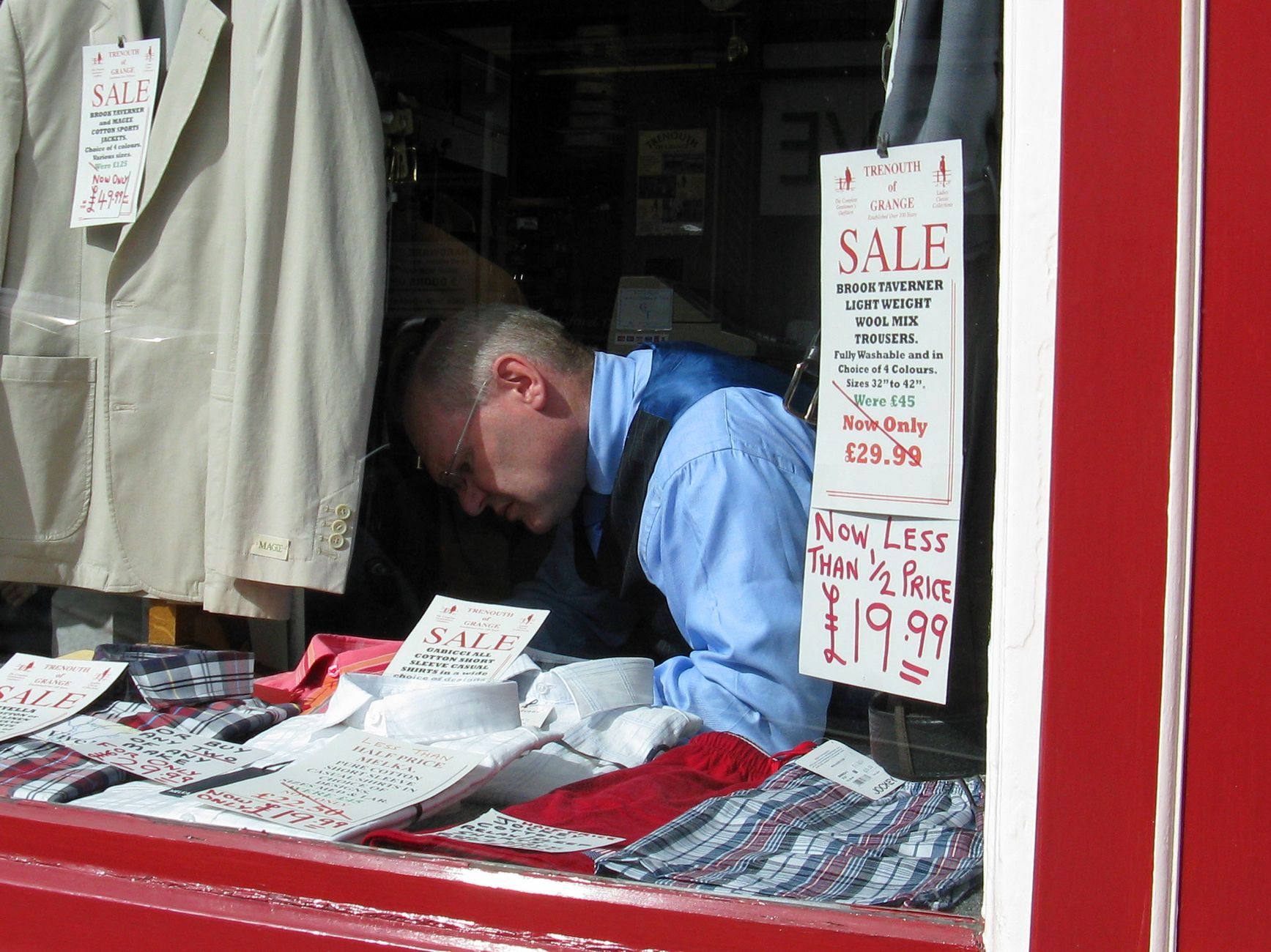 A welcoming shop window displays a clear first-visit offer sign as passing customers stop to read it.