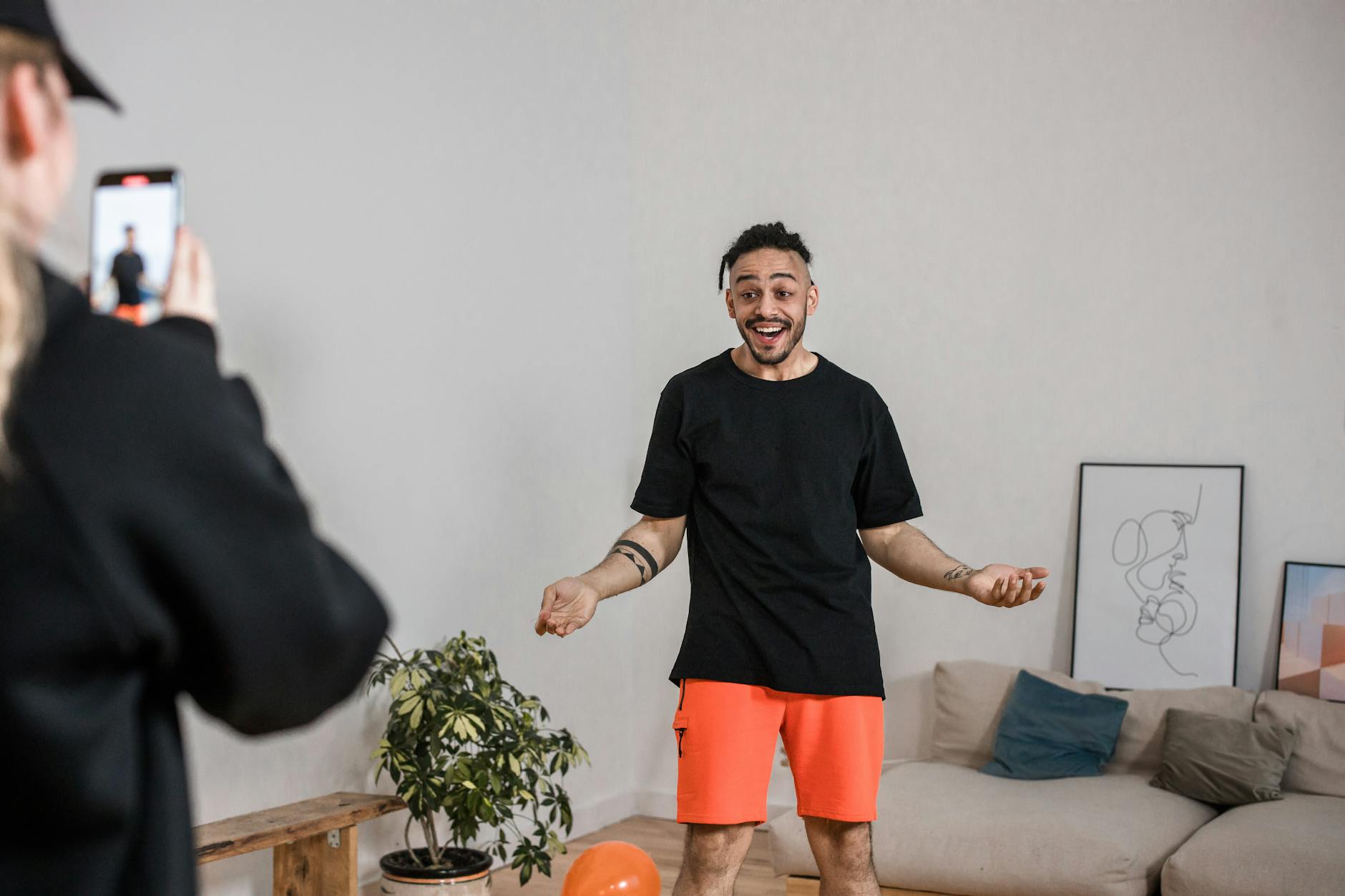 Man in black shirt vlogging indoors with smartphone capturing lively expressions.