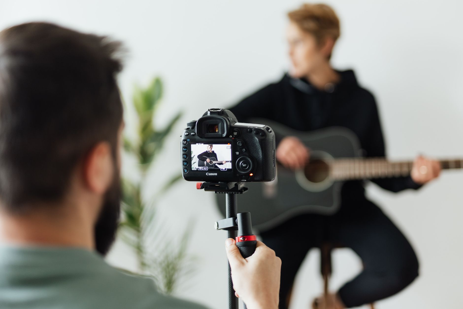 A young musician records a vertical short-form video performing a hook to a phone on a tripod in a bright room.