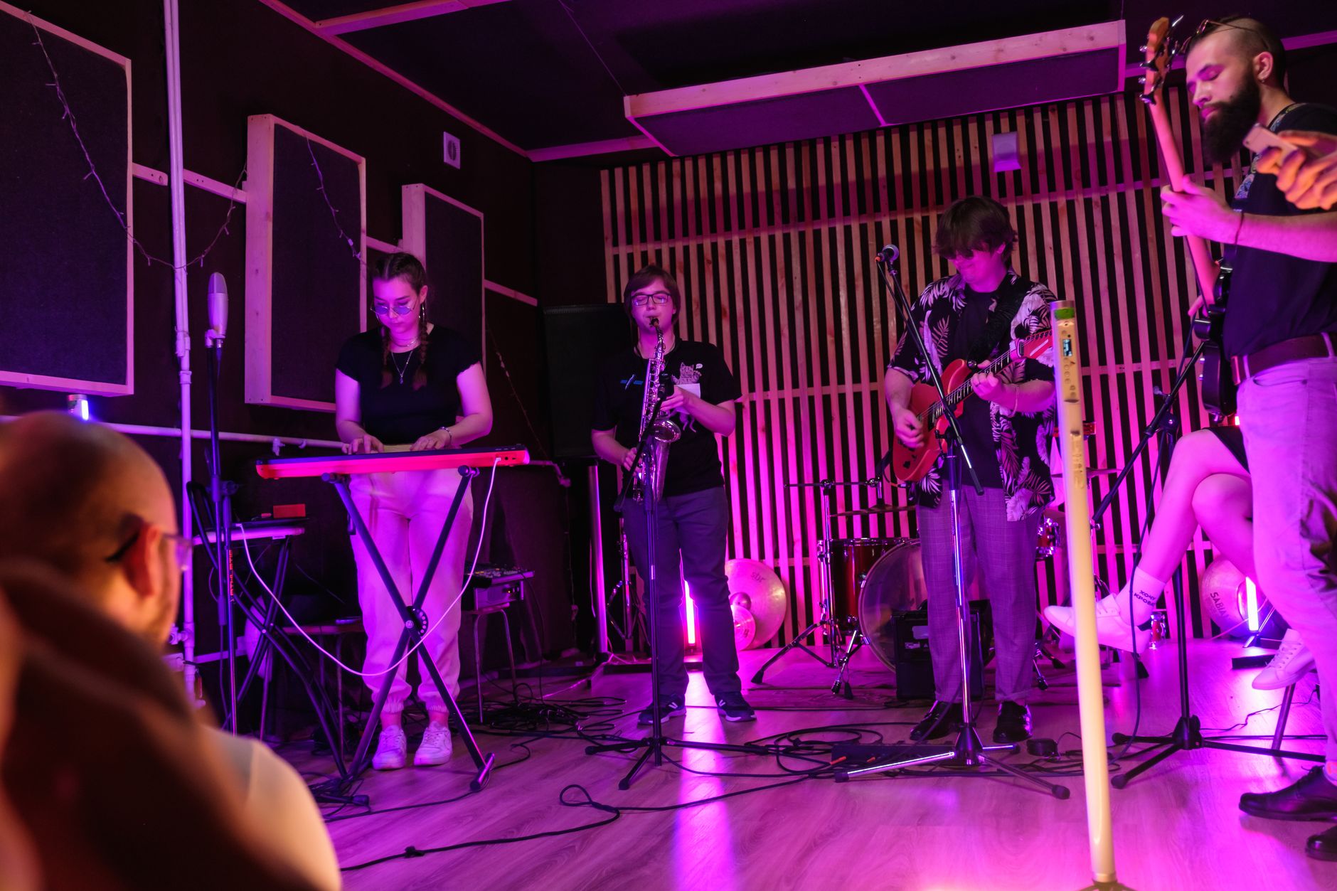 A band plays to an engaged crowd in a small local live music venue, lit by warm stage lights.