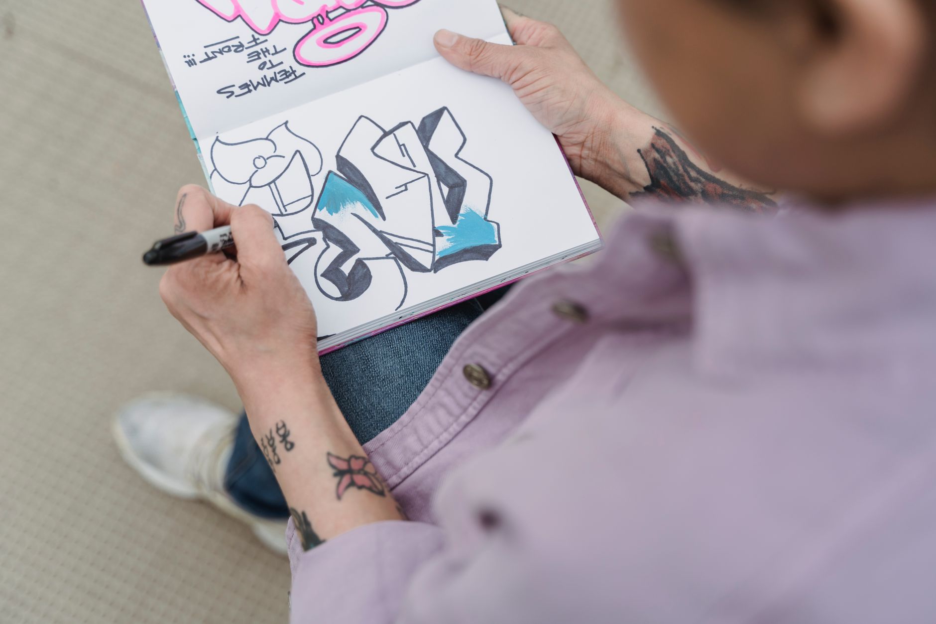 An artist writes notes in a notebook beside a finished piece, drafting the short story and description that will accompany the listing.