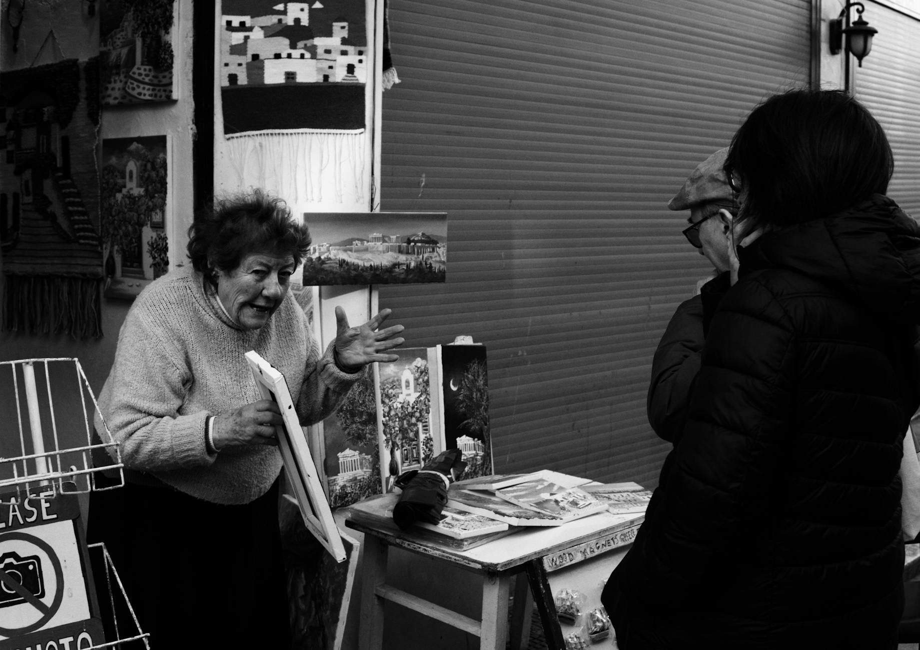 A street market vendor passionately explains artwork to two visitors, showcasing vibrant local art.
