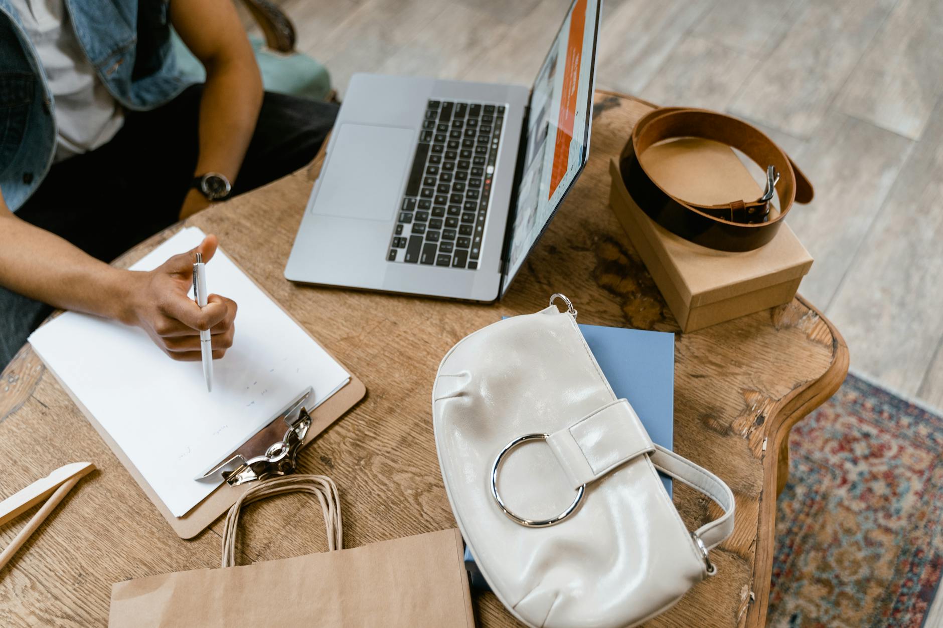 A stylish workspace featuring a laptop, handbag, and office supplies on a wooden table.