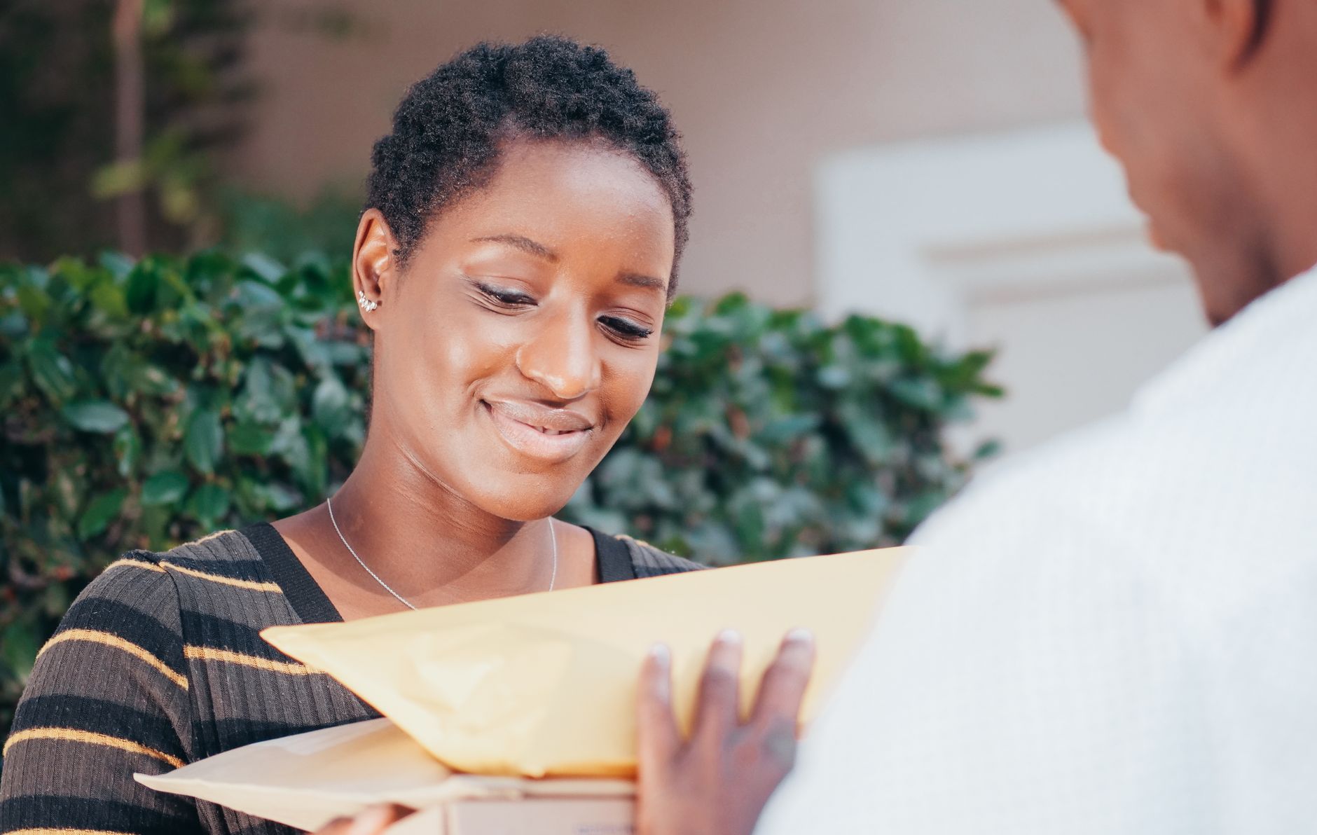 A delighted customer opens a carefully packaged handmade parcel at a kitchen table, lifting out a candle wrapped with a handwritten thank-you note.