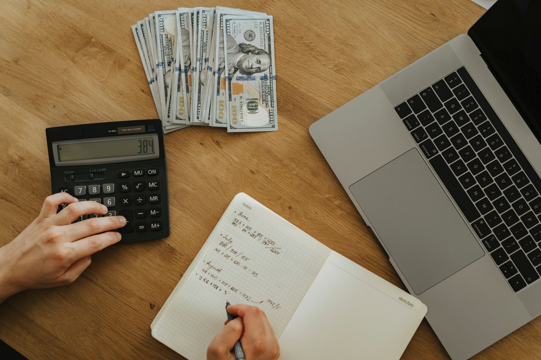 Hands using a calculator beside a notebook while working out cleaning job prices