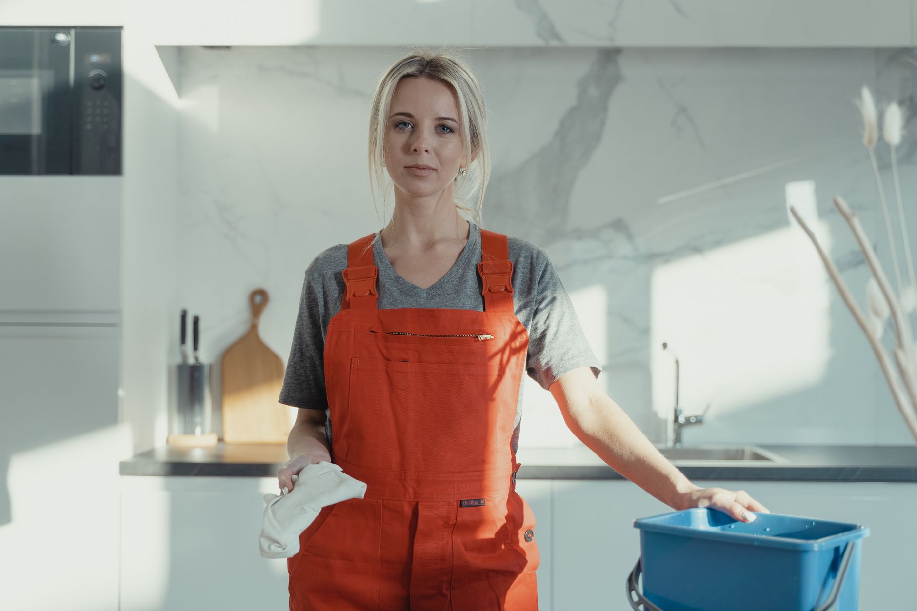 A professional cleaner in an apron wiping down a bright, tidy kitchen worktop