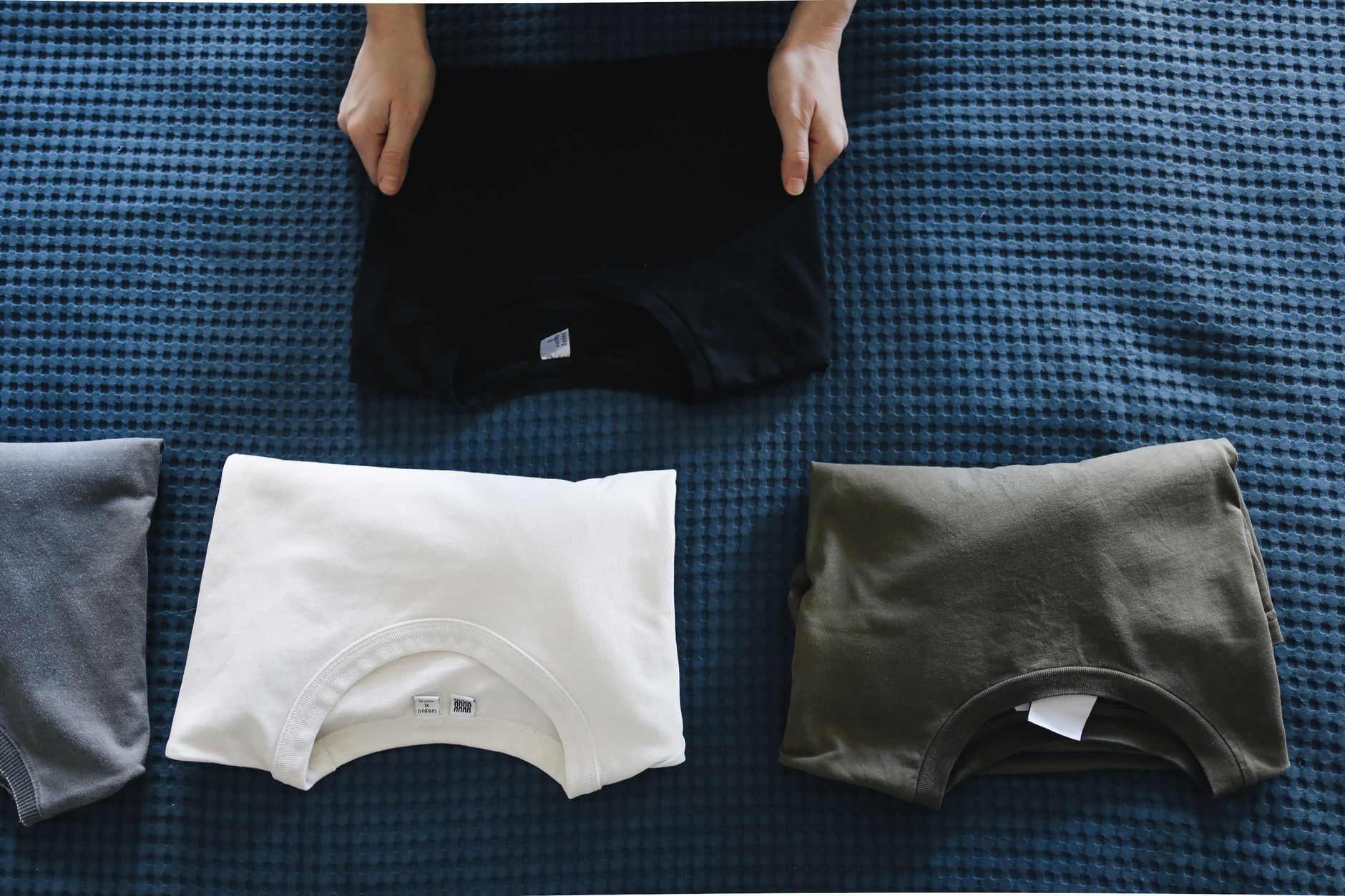 A person folding freshly printed t shirts at a worktable, choosing a clothing model