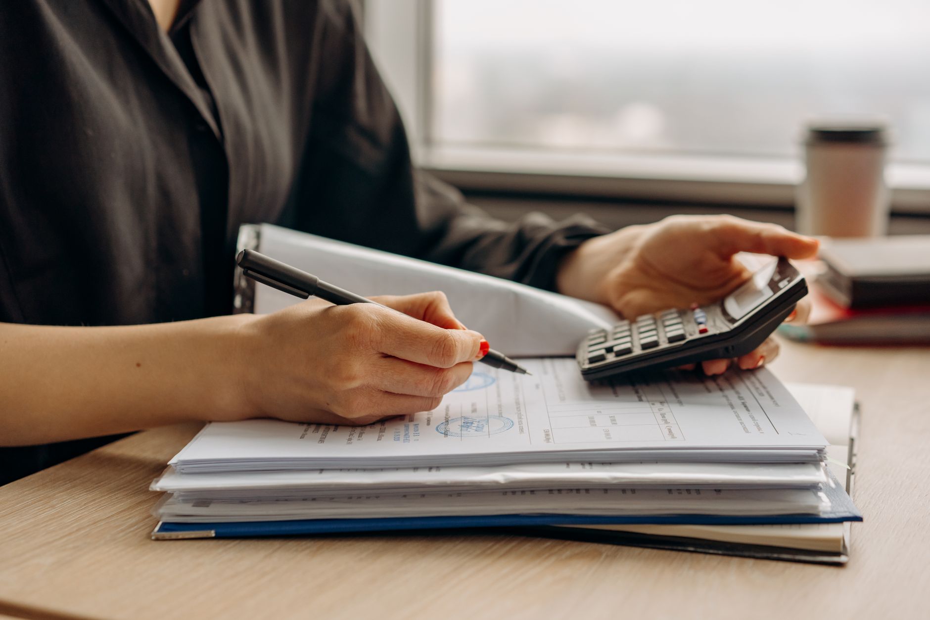 A person working through paperwork with a calculator and notebook at a desk