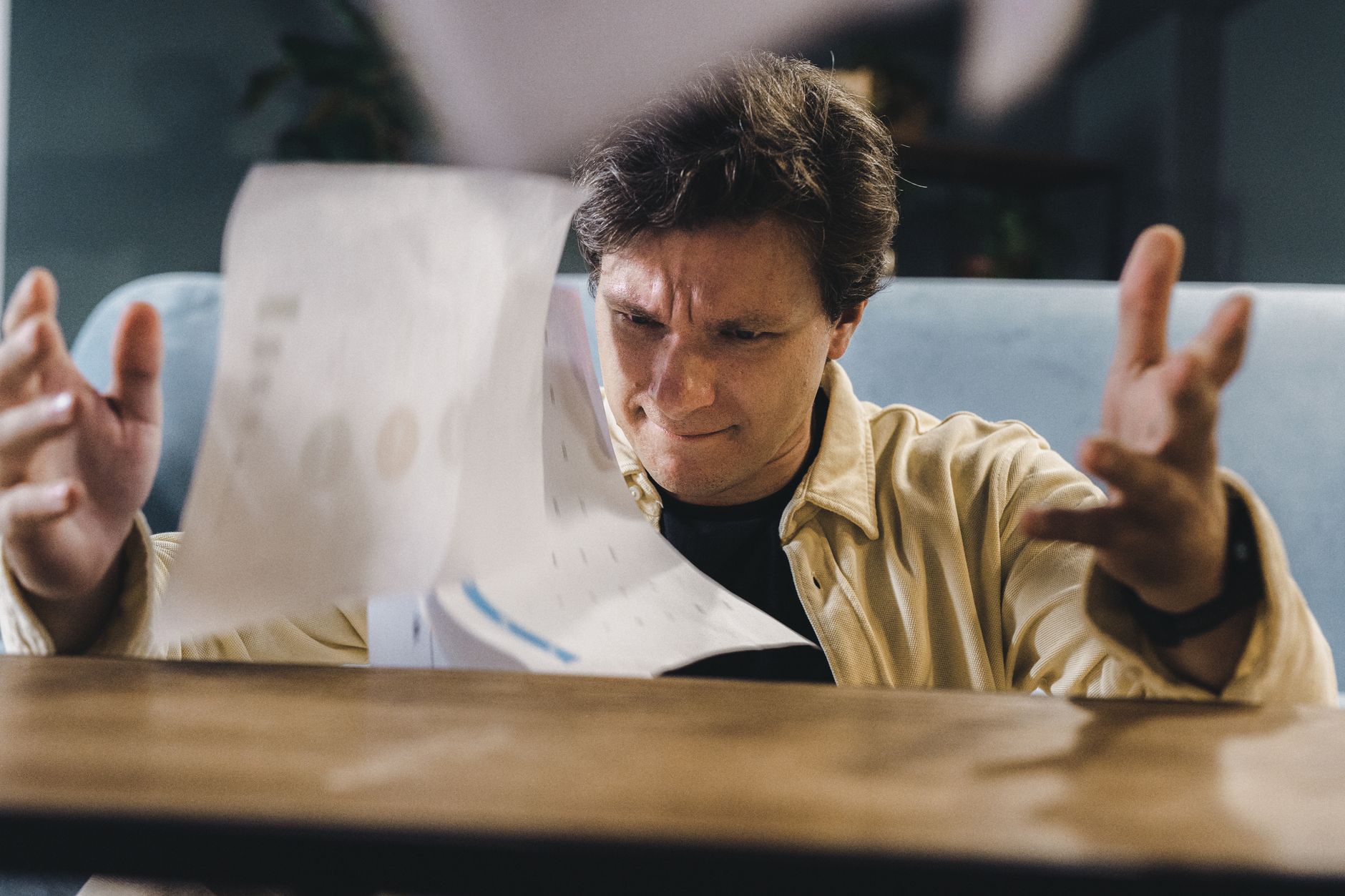 A stressed man holding his head at a cluttered desk surrounded by paperwork