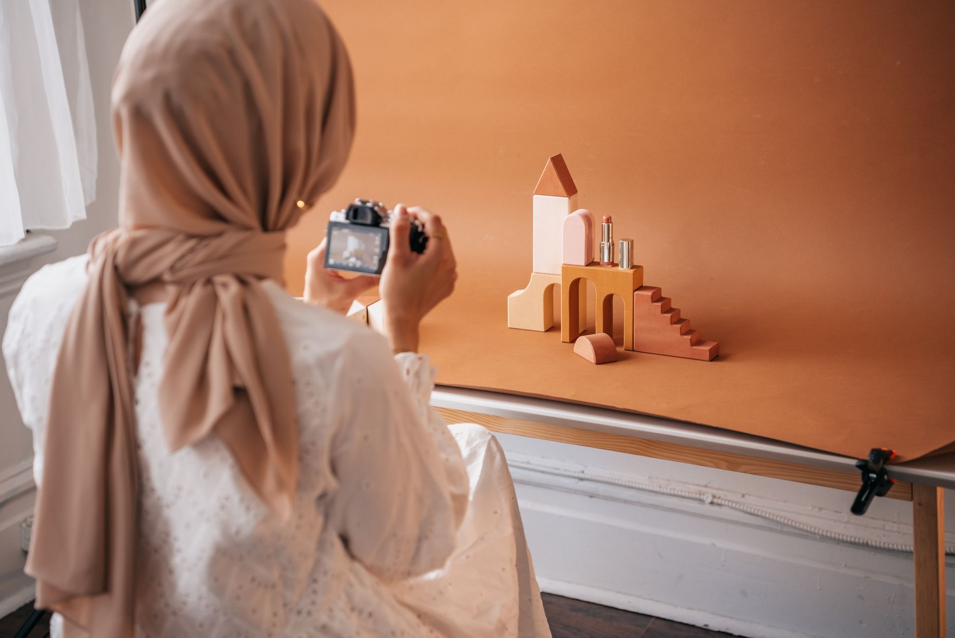 A shop owner photographs a product on a phone for a social channel, styling it against a clean background near a window.
