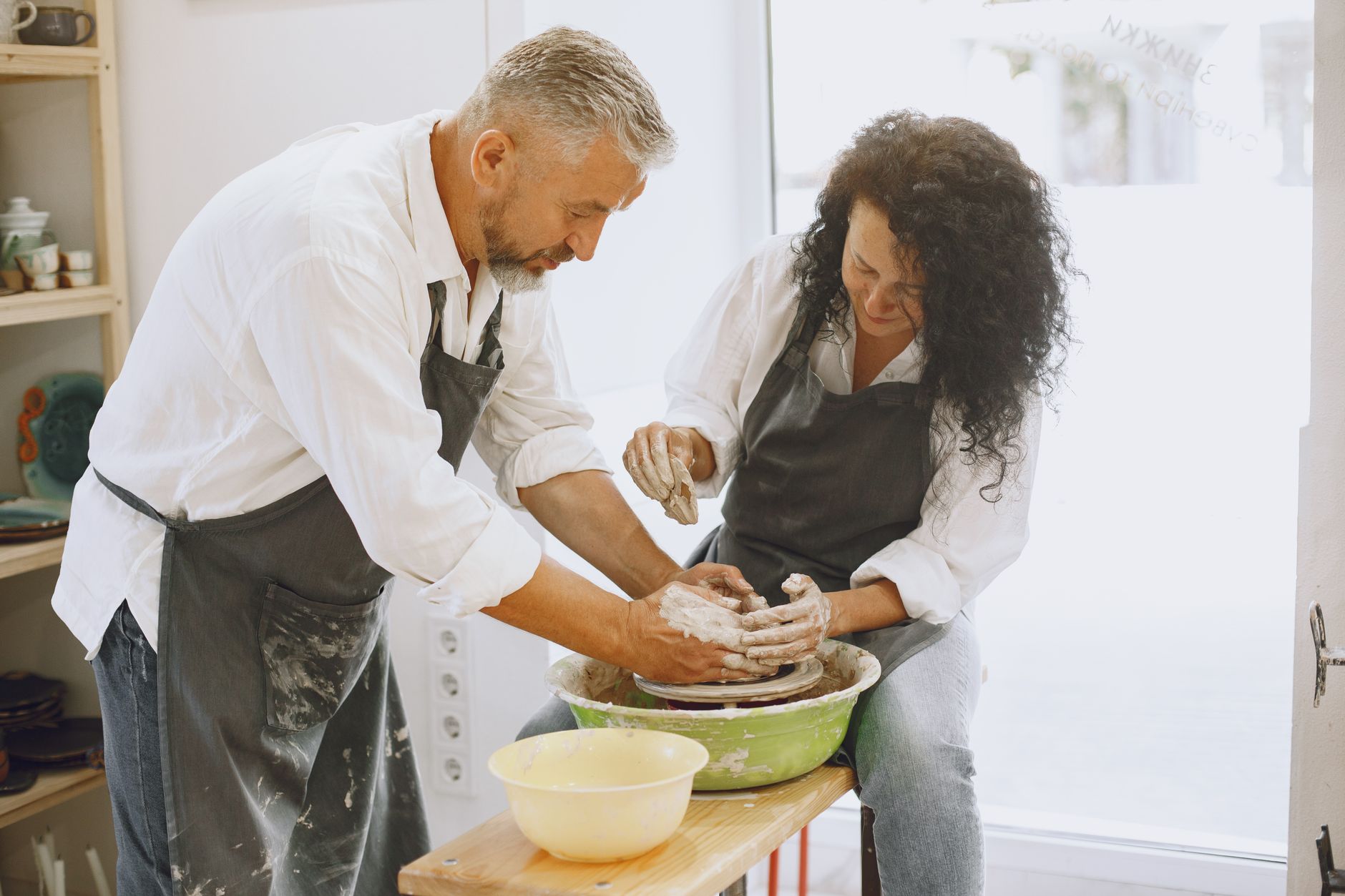 A pottery teacher working closely with a beginner student