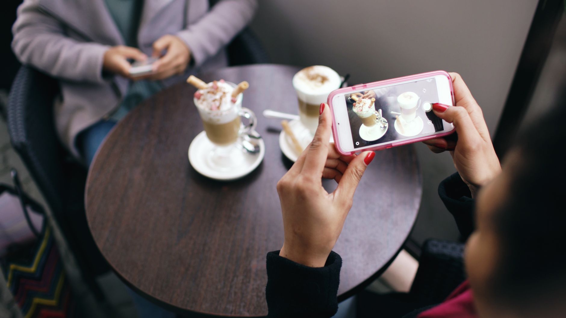 Two friends photographing their coffees at a cafe table