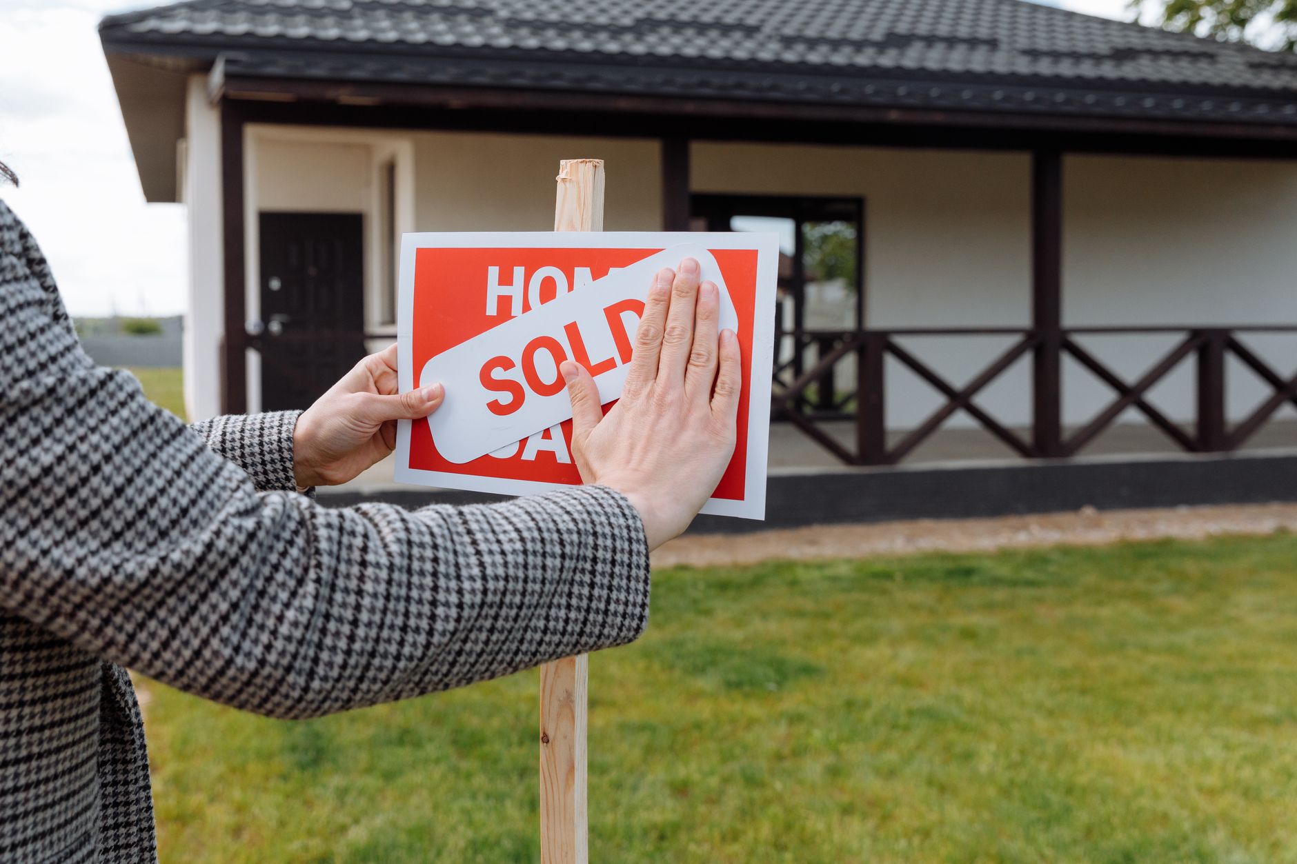 Two neighbours talking near a house with a sold sign outside