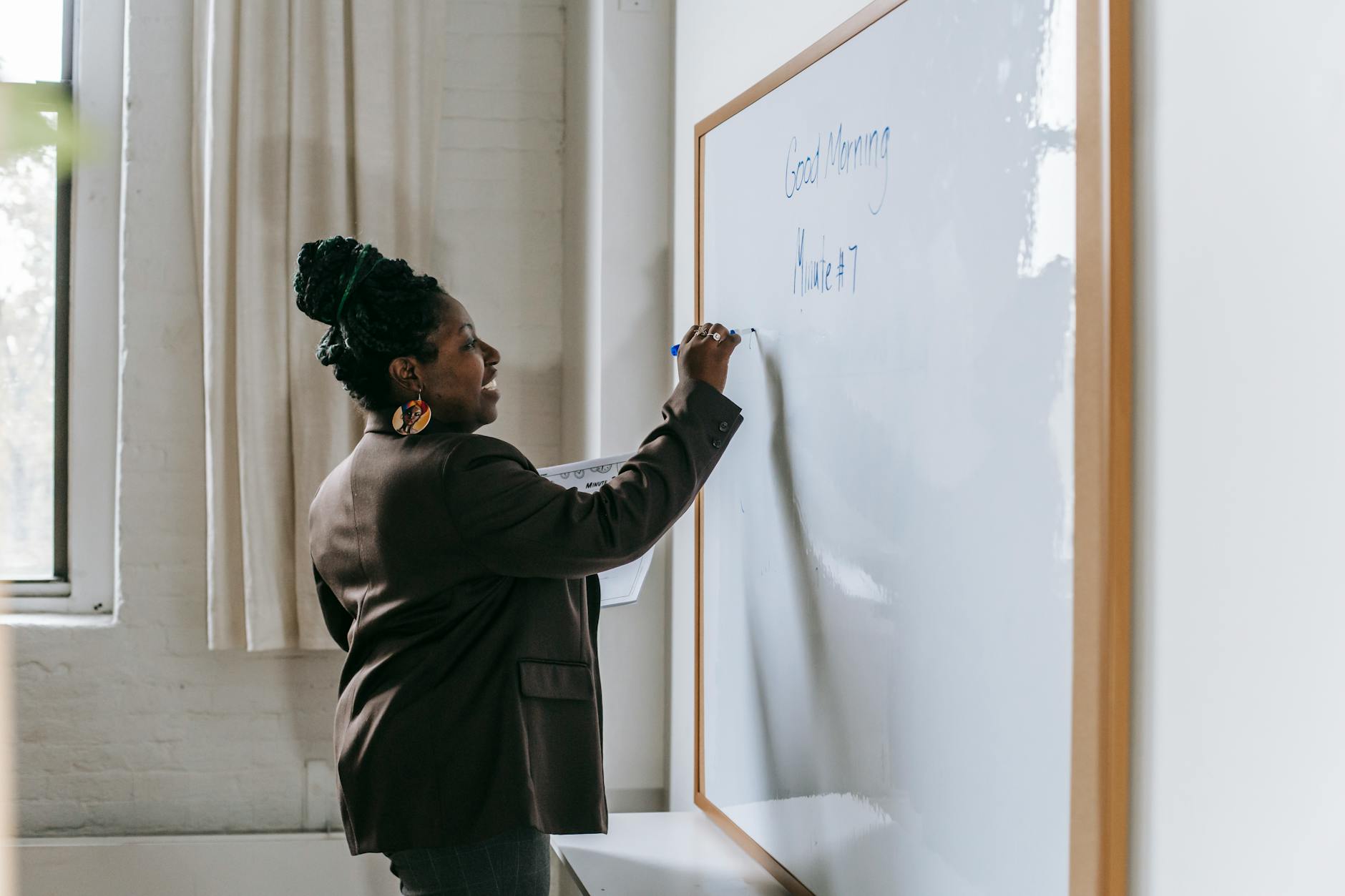 Side view of smiling African American woman writing on whiteboard standing in modern school classroom