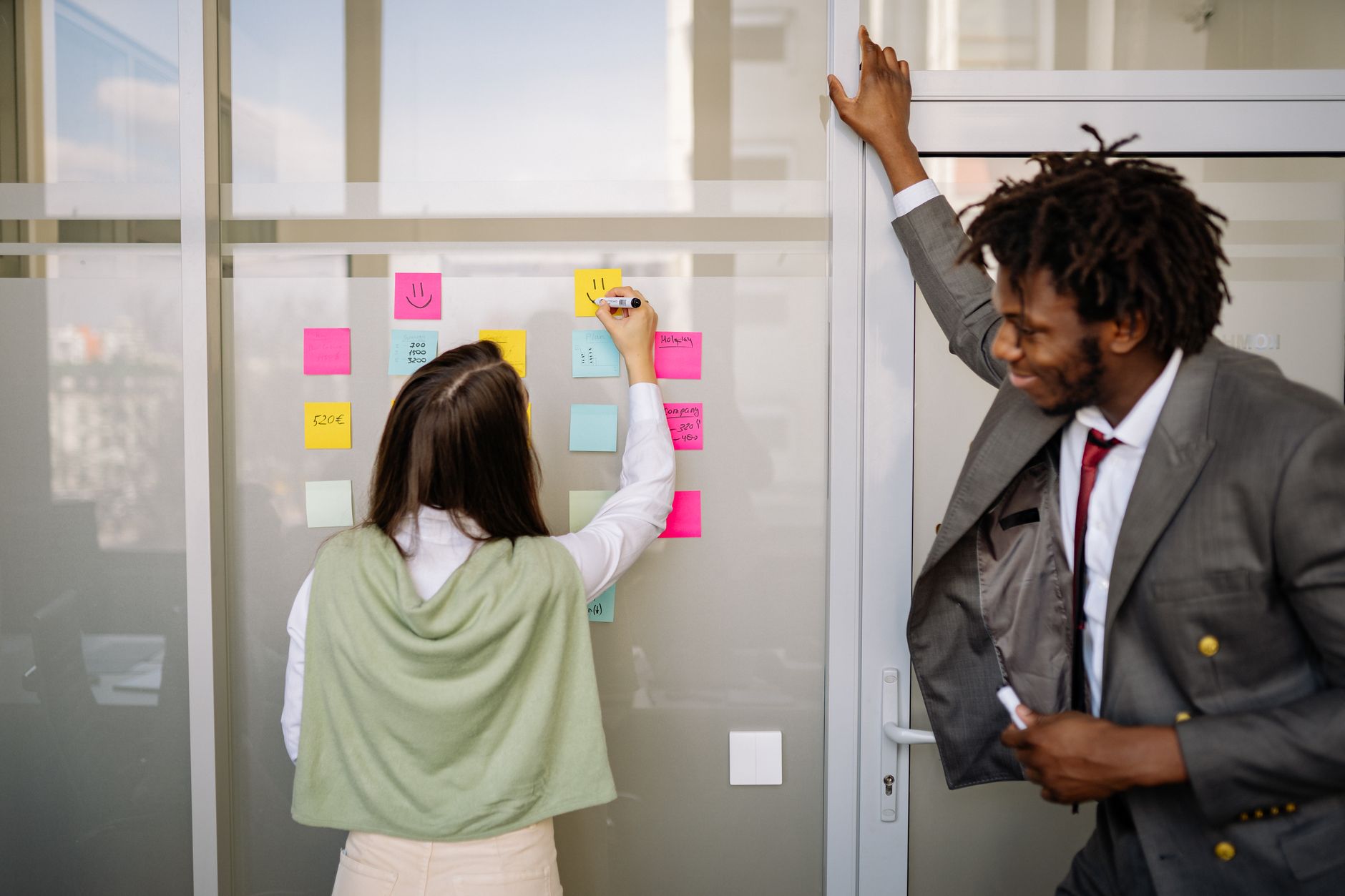 Two colleagues planning together with sticky notes on a wall