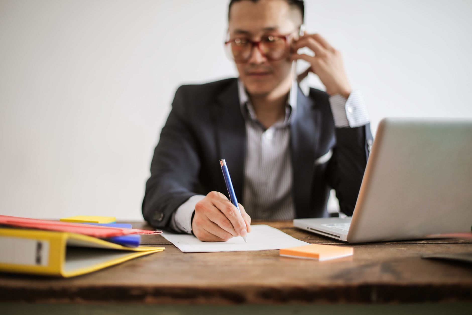 A man on a phone call taking notes at his desk