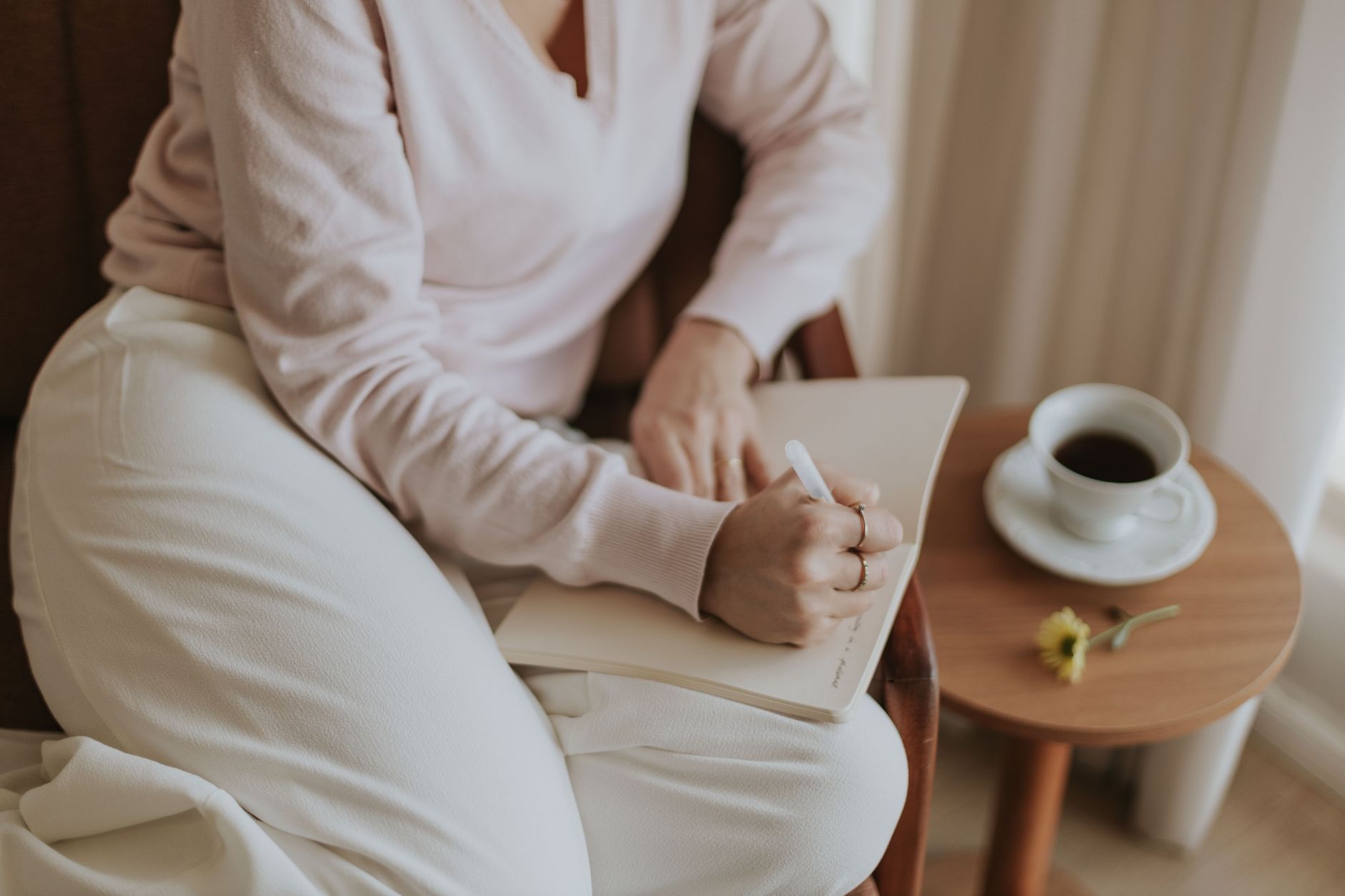 A person thinking and writing in a notebook with a coffee at home