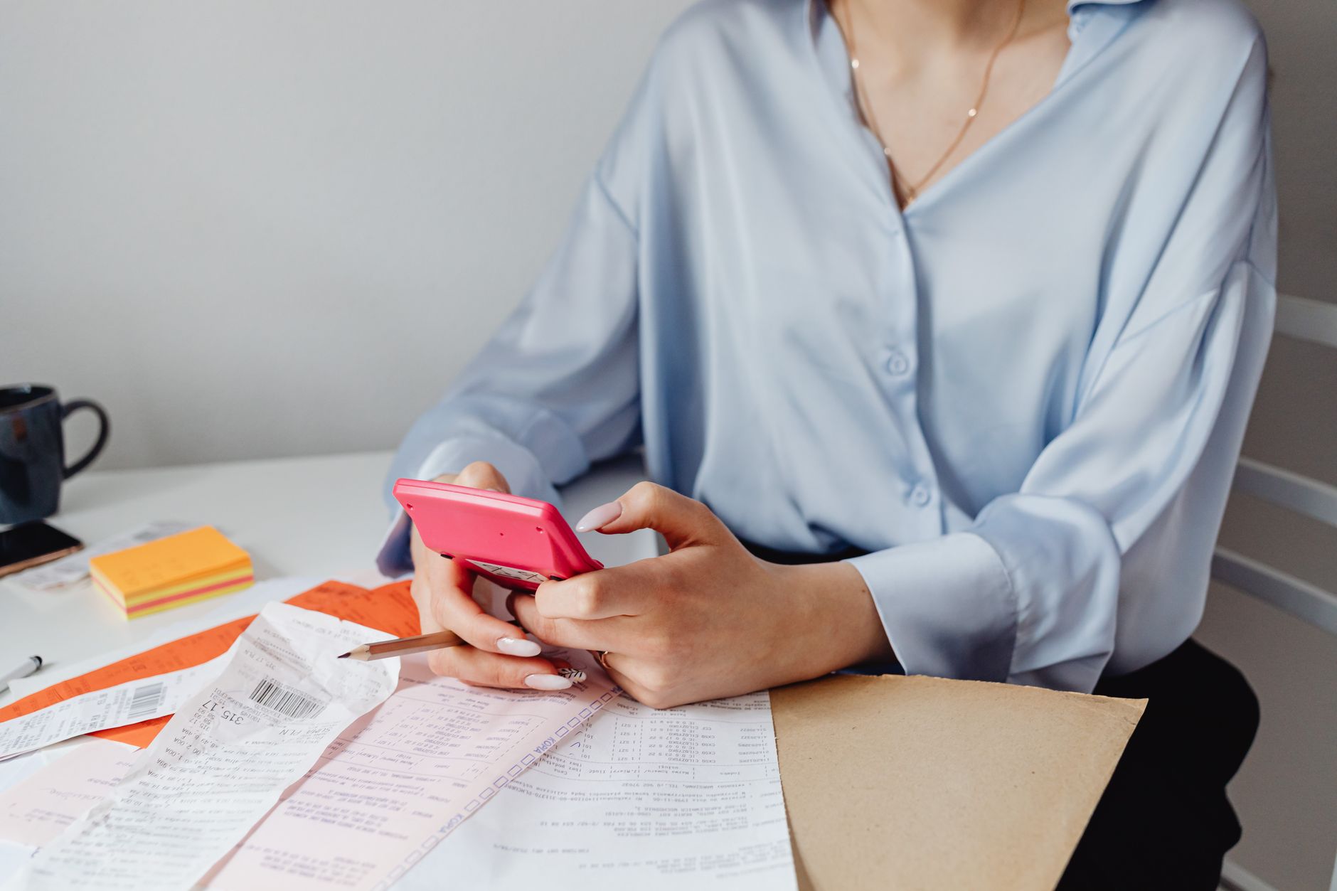 A person sorting paper receipts with a calculator at a kitchen table