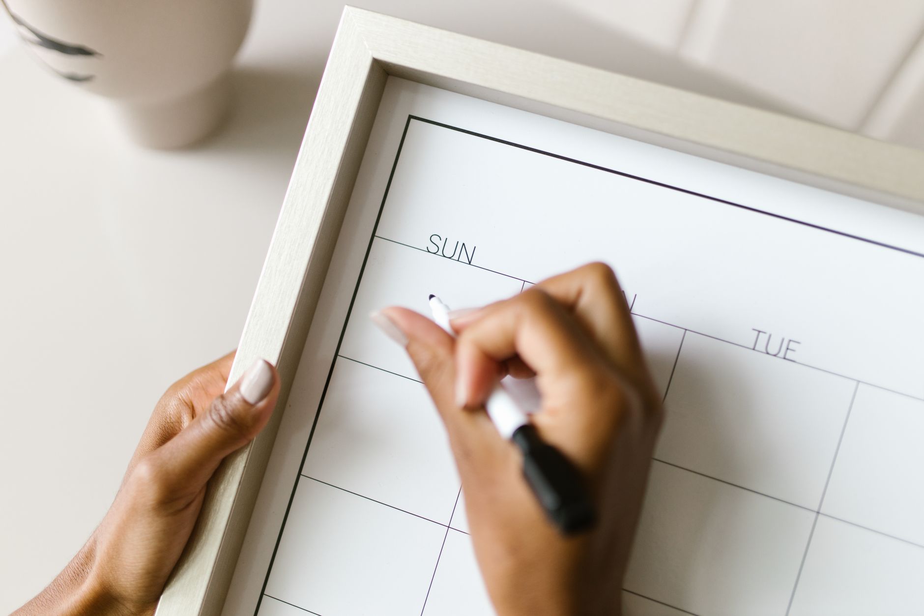 A woman writing plans for the month ahead on a wall calendar at home
