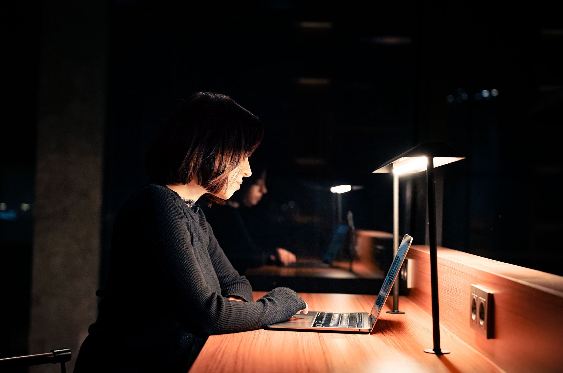 A woman working on her side hustle at a home desk in the evening by lamplight