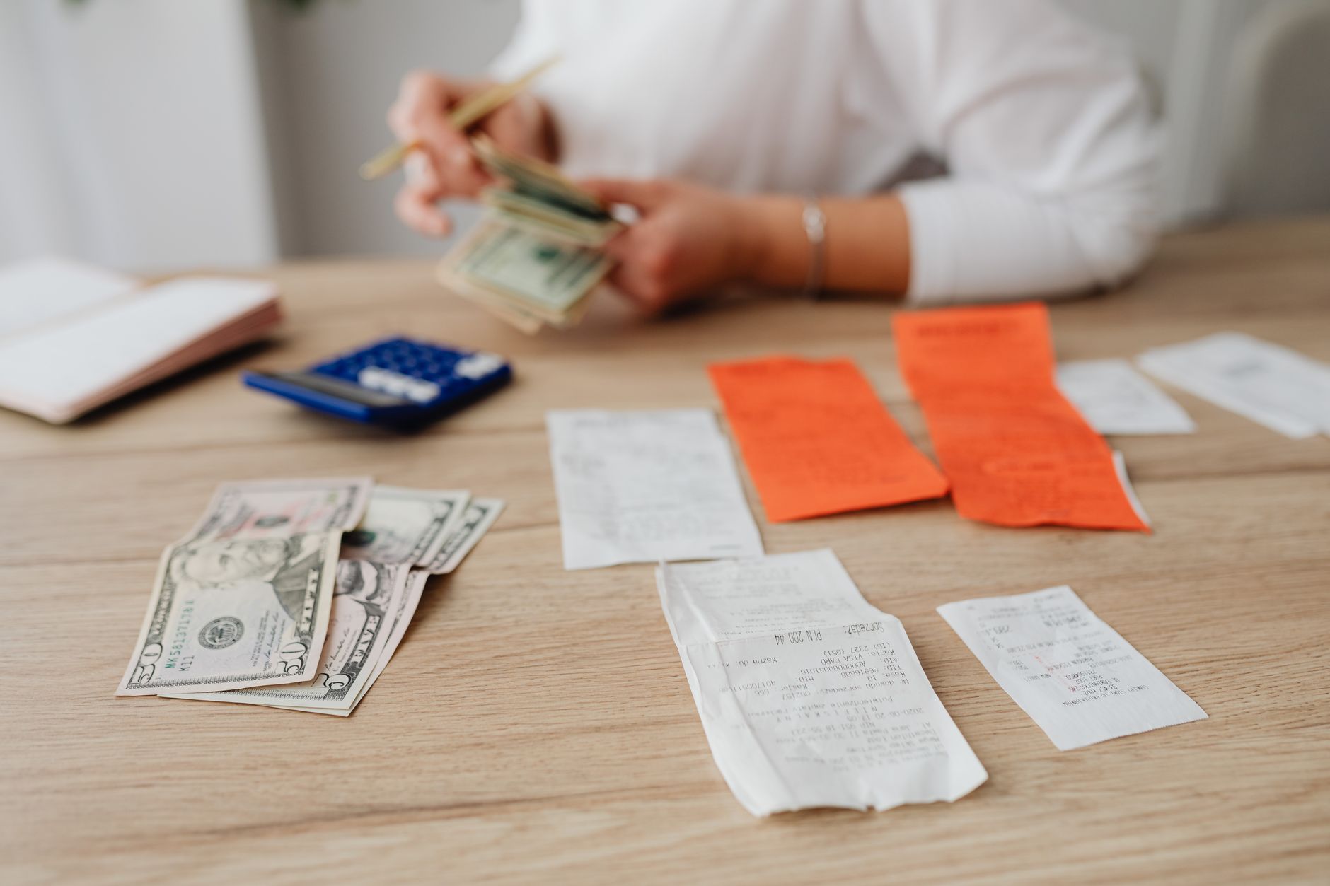 A person sorting paper receipts with a calculator and notebook at a kitchen table